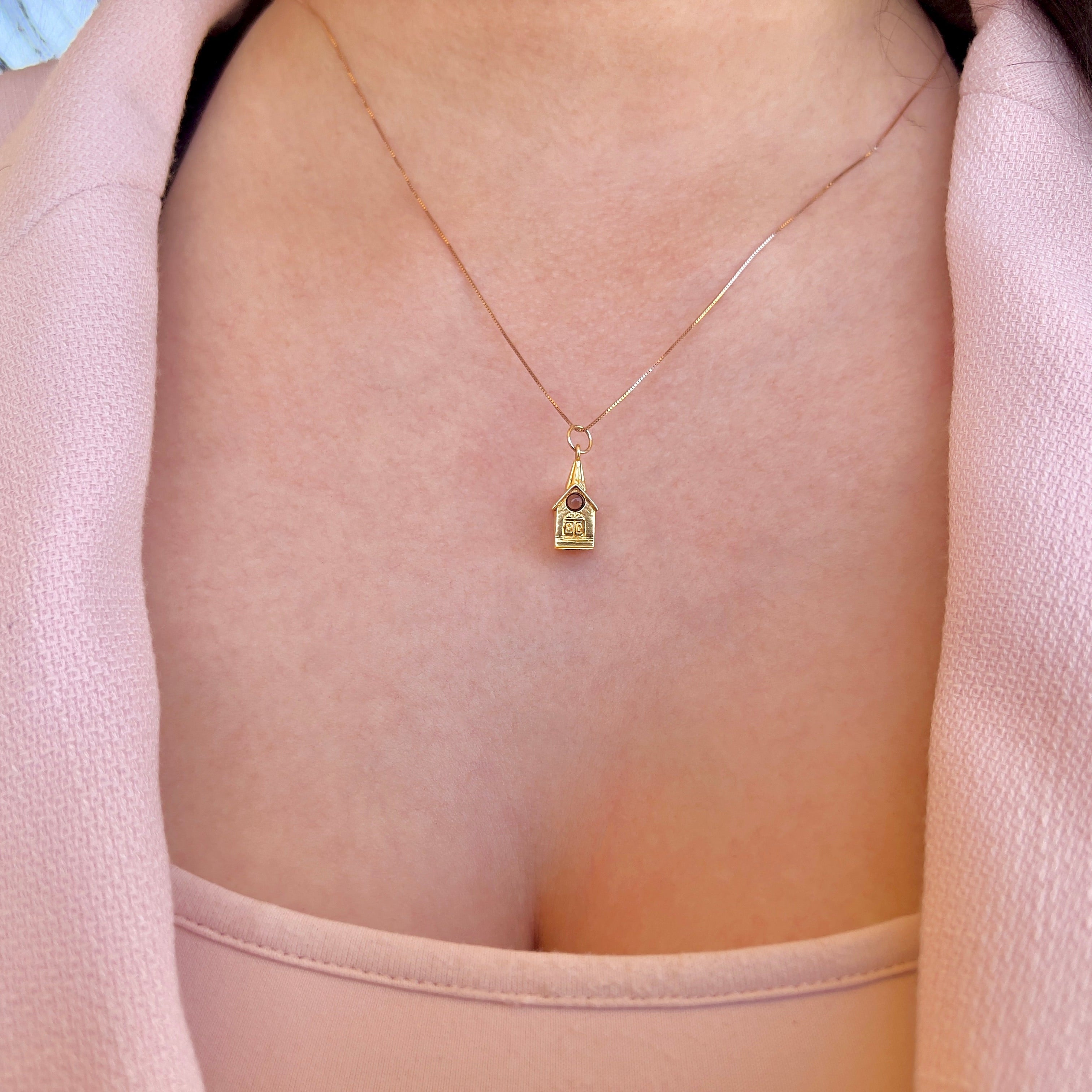 A close up of a person wearing a gold chain with a chapel charm. 