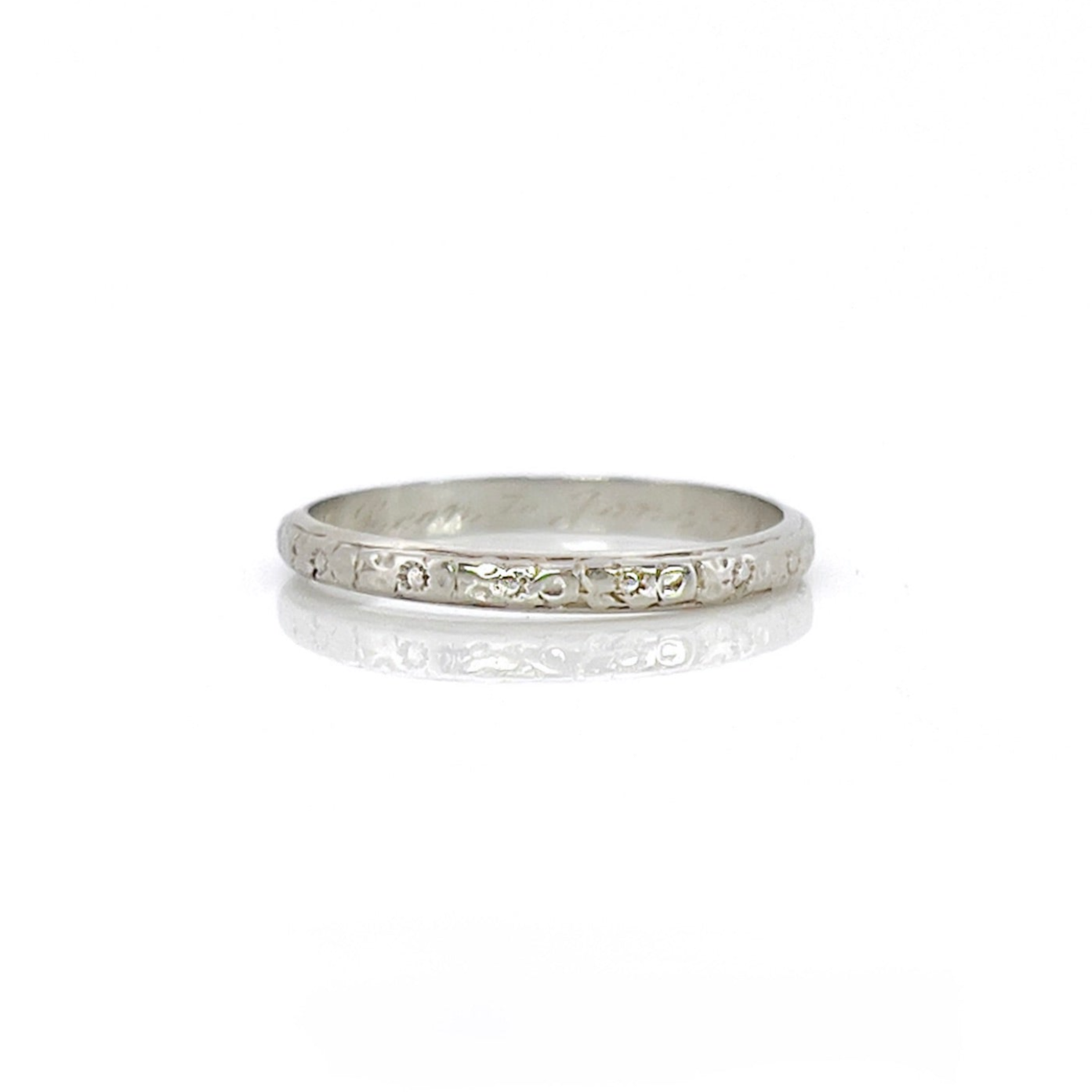 A vintage 14K white gold wedding band with an intricate floral design and personalized engraving inside.