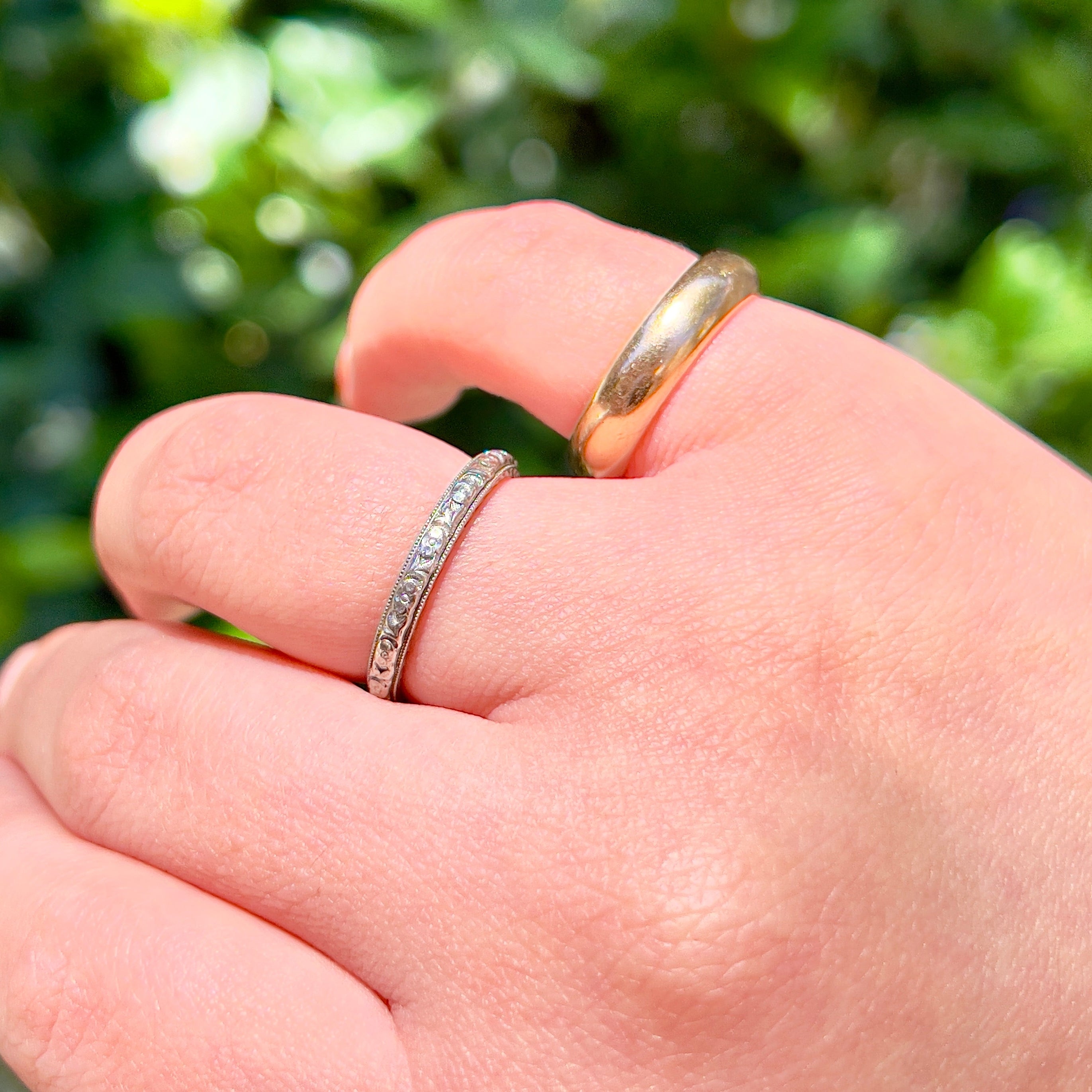 Silver and gold rings on a hand with green background.