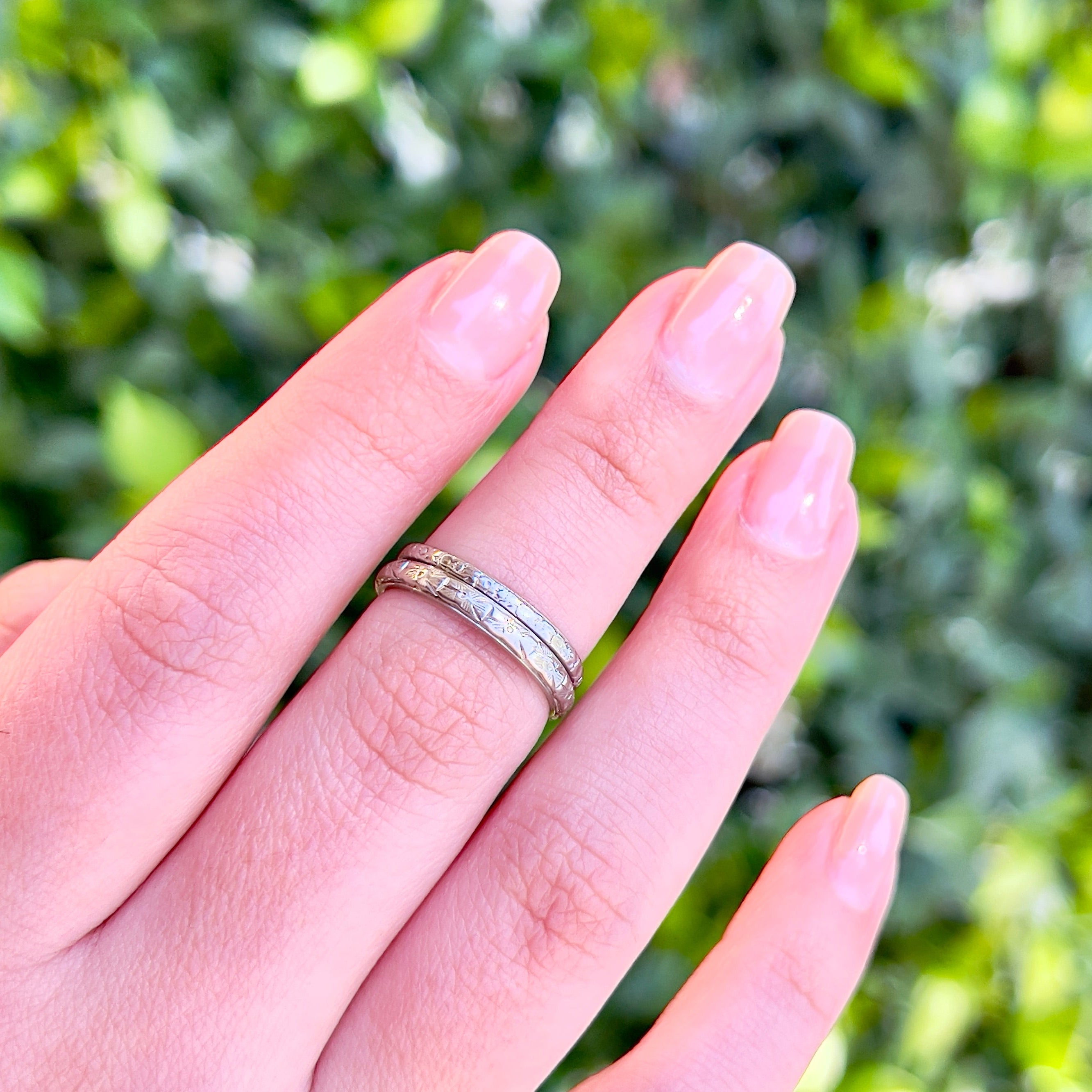 Two vintage white gold wedding bands modeled on a middle finger against an outdoor background.