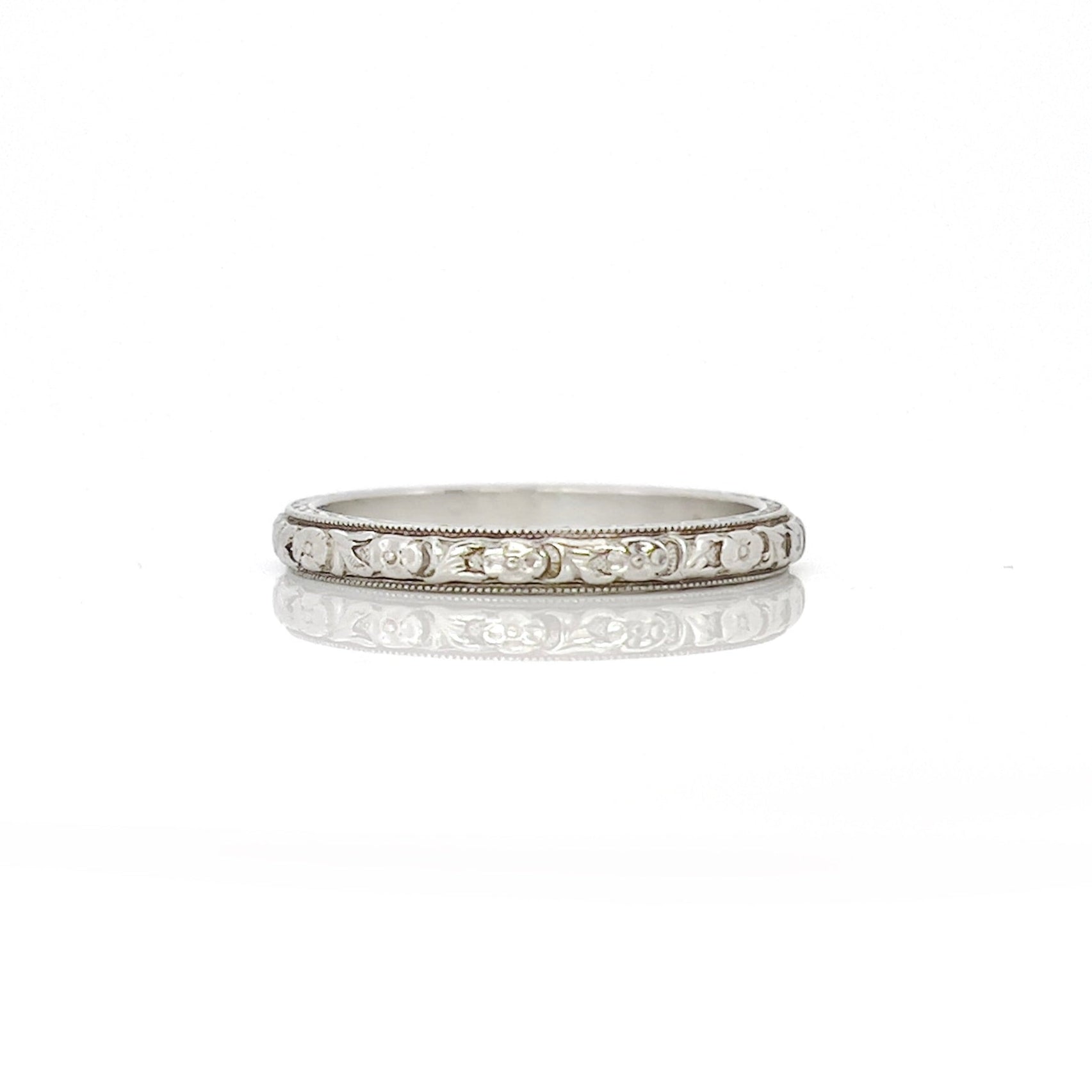 An white gold and platinum vintage wedding band with a floral design, engraved details on the sides, displayed against a white background.