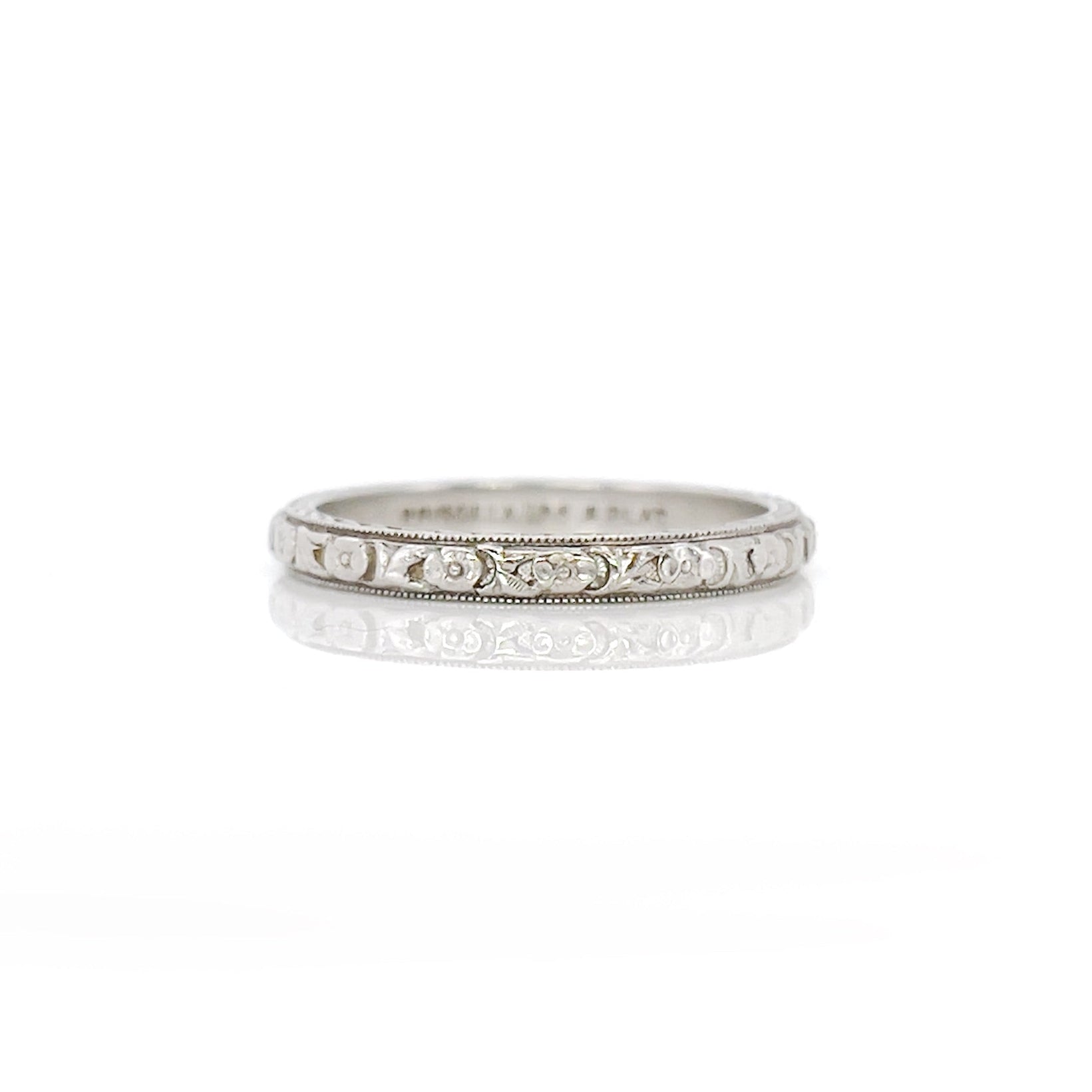 An white gold and platinum vintage wedding band with a floral design, engraved details on the sides, displayed against a white background.