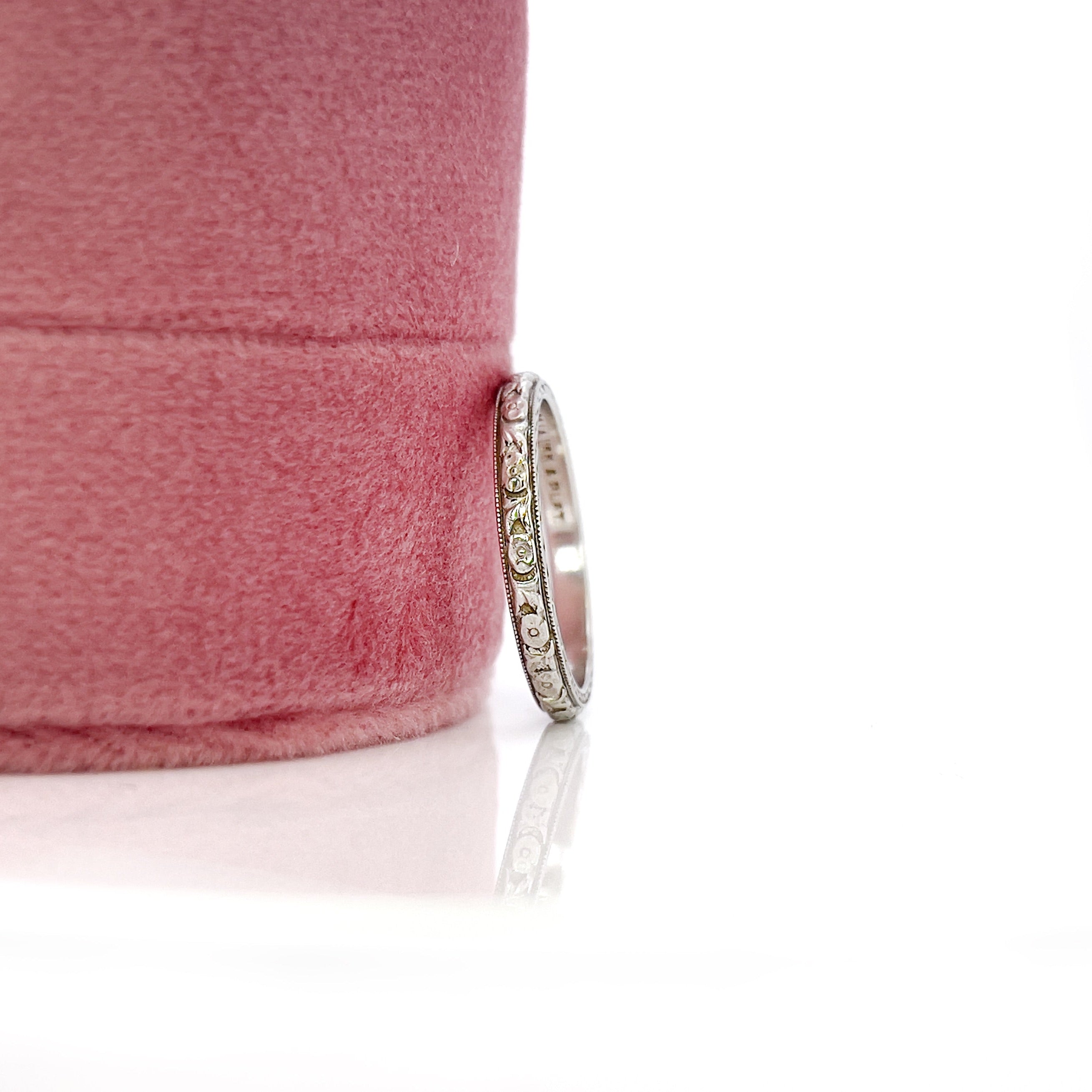 An white gold and platinum vintage wedding band with a floral design, engraved details on the sides, displayed against a white background.