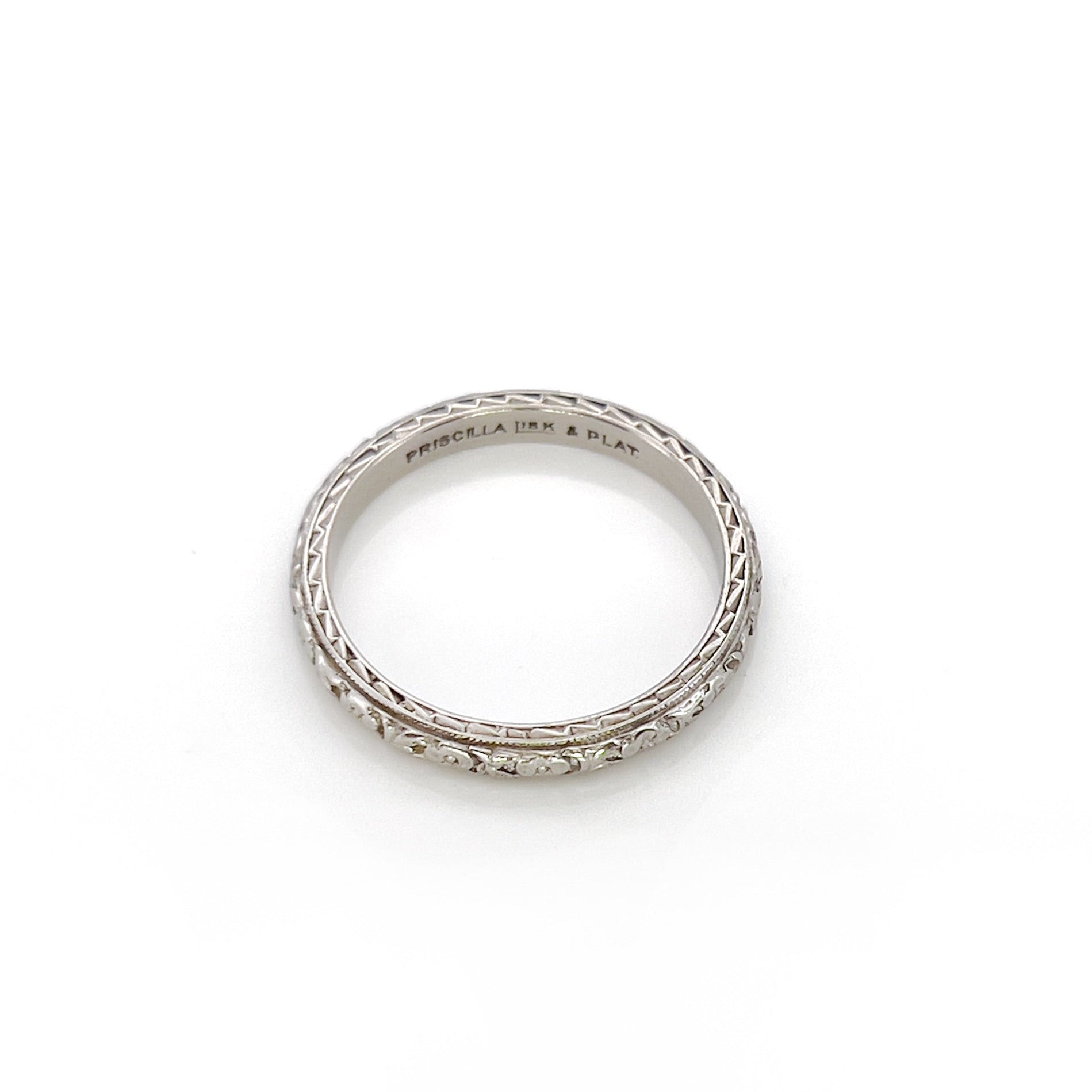 An white gold and platinum vintage wedding band with a floral design, engraved details on the sides, displayed against a white background.