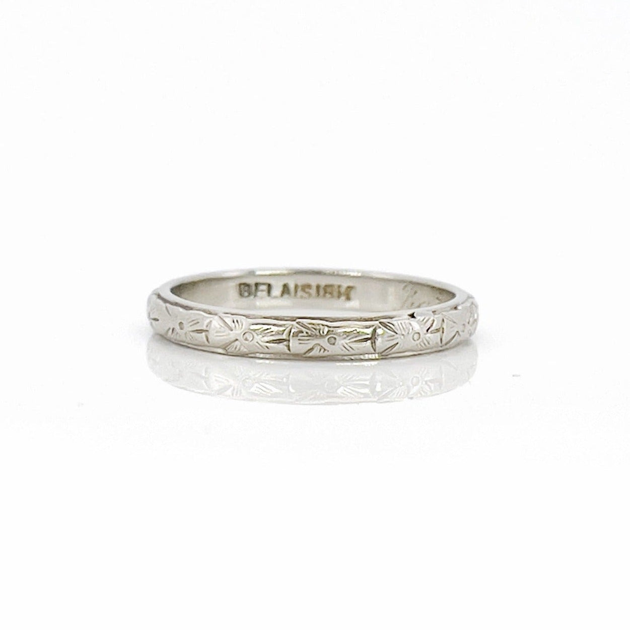A vintage white gold wedding band with an intricate floral design and the name 'Berta' engraved inside.