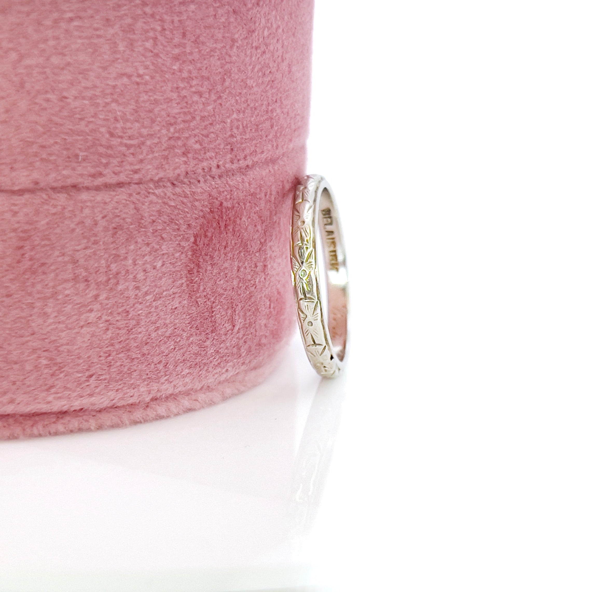 A vintage white gold wedding band with an intricate floral design and the name 'Berta' engraved inside.