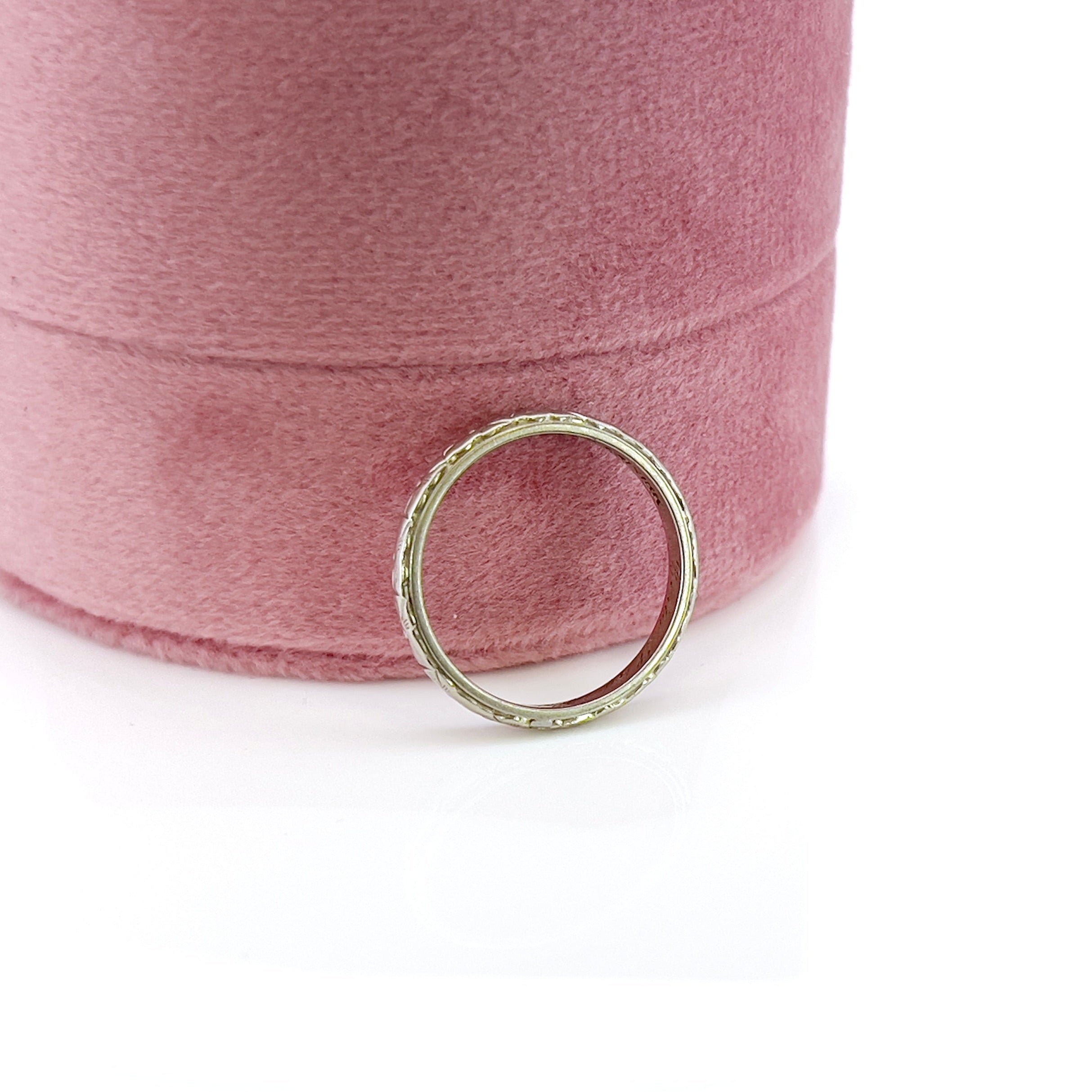 A vintage white gold wedding band with an intricate floral design and the name 'Berta' engraved inside.