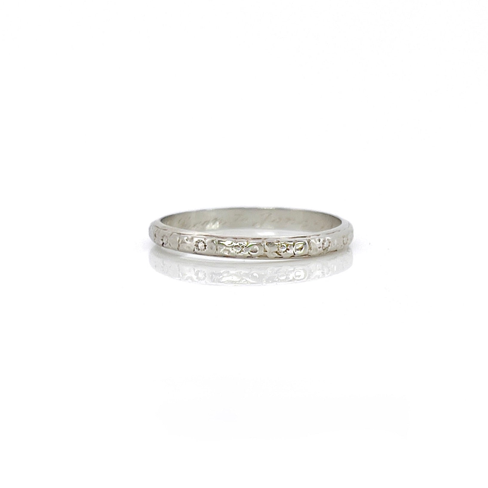 A vintage 14K white gold wedding band with an intricate floral design and personalized engraving inside.