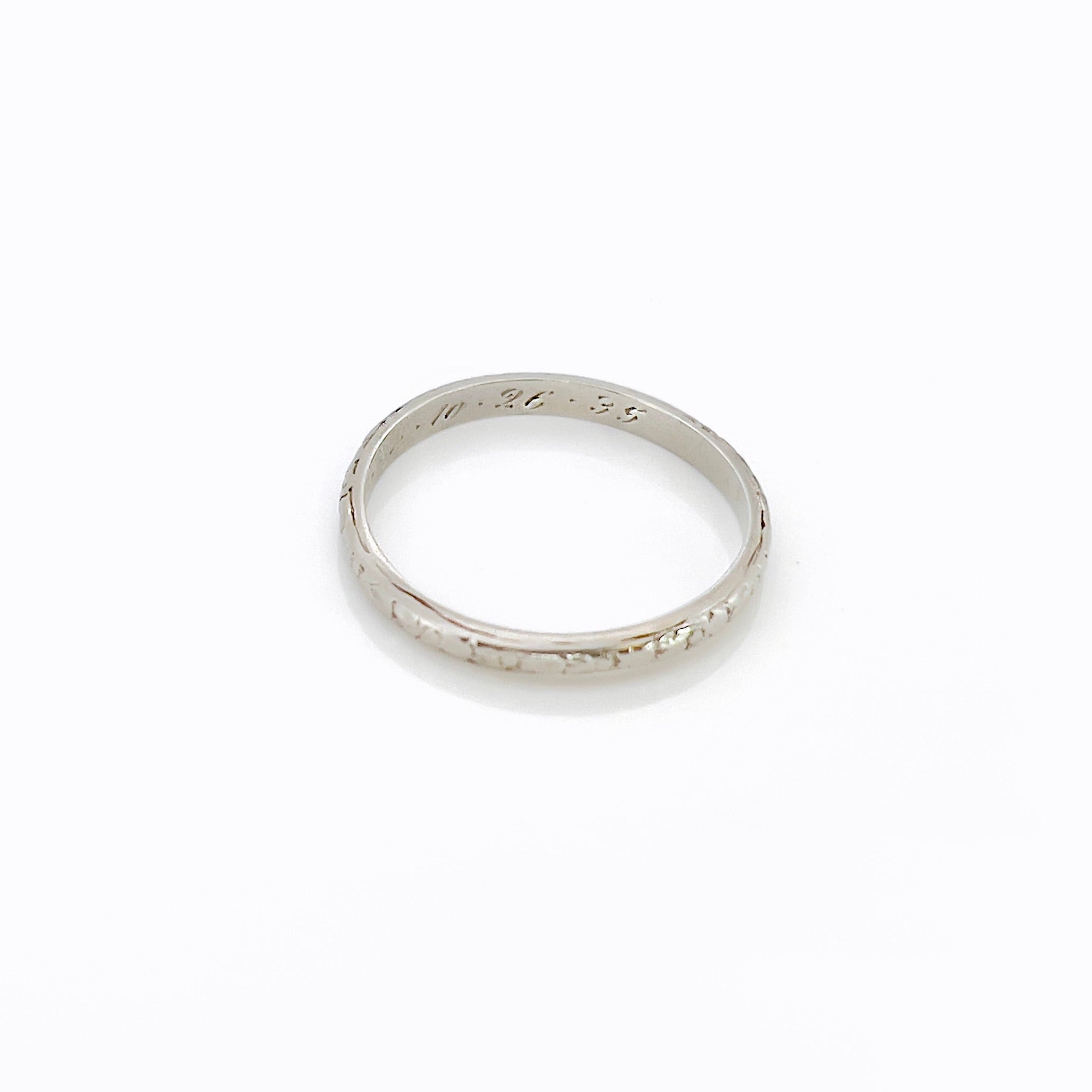 A vintage 14K white gold wedding band with an intricate floral design and personalized engraving inside.