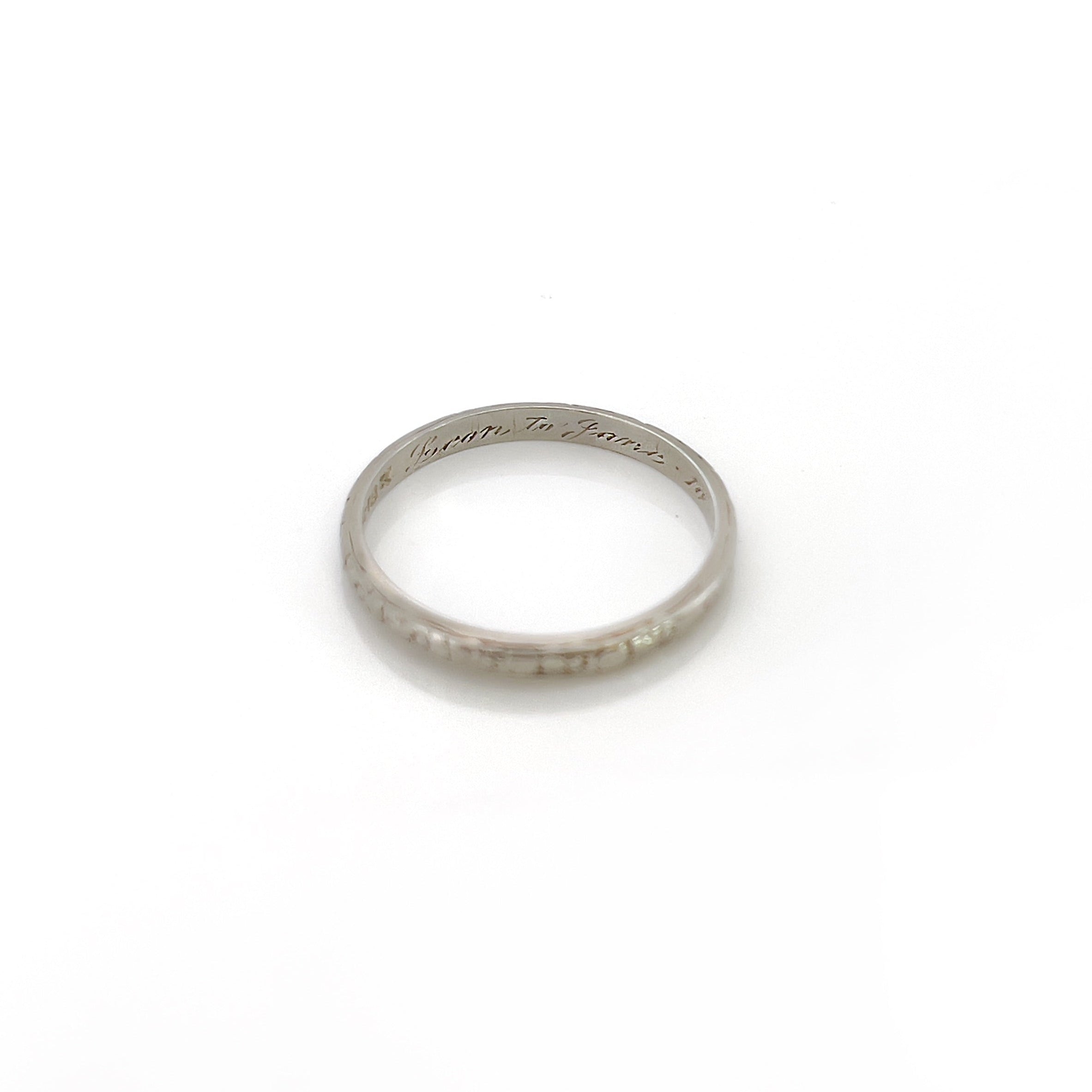 A vintage 14K white gold wedding band with an intricate floral design and personalized engraving inside.