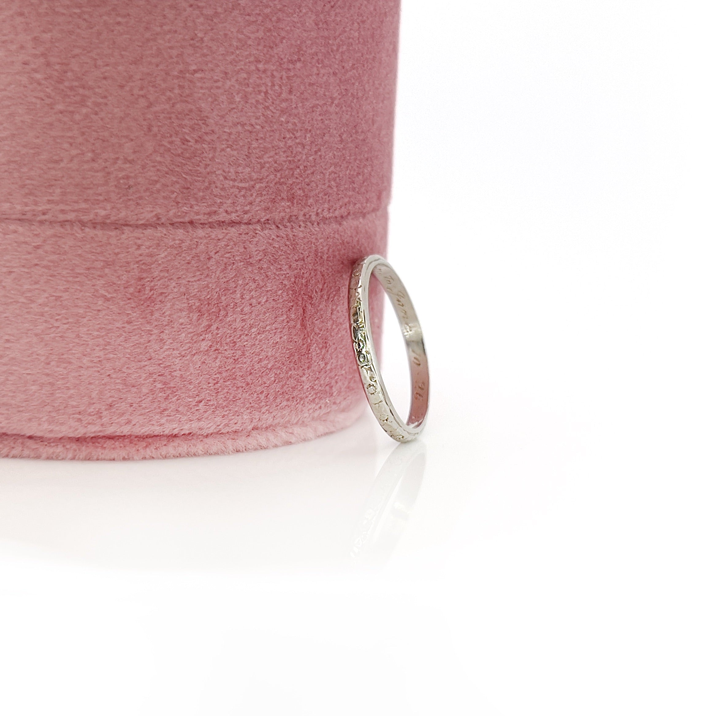A vintage 14K white gold wedding band with an intricate floral design and personalized engraving inside.