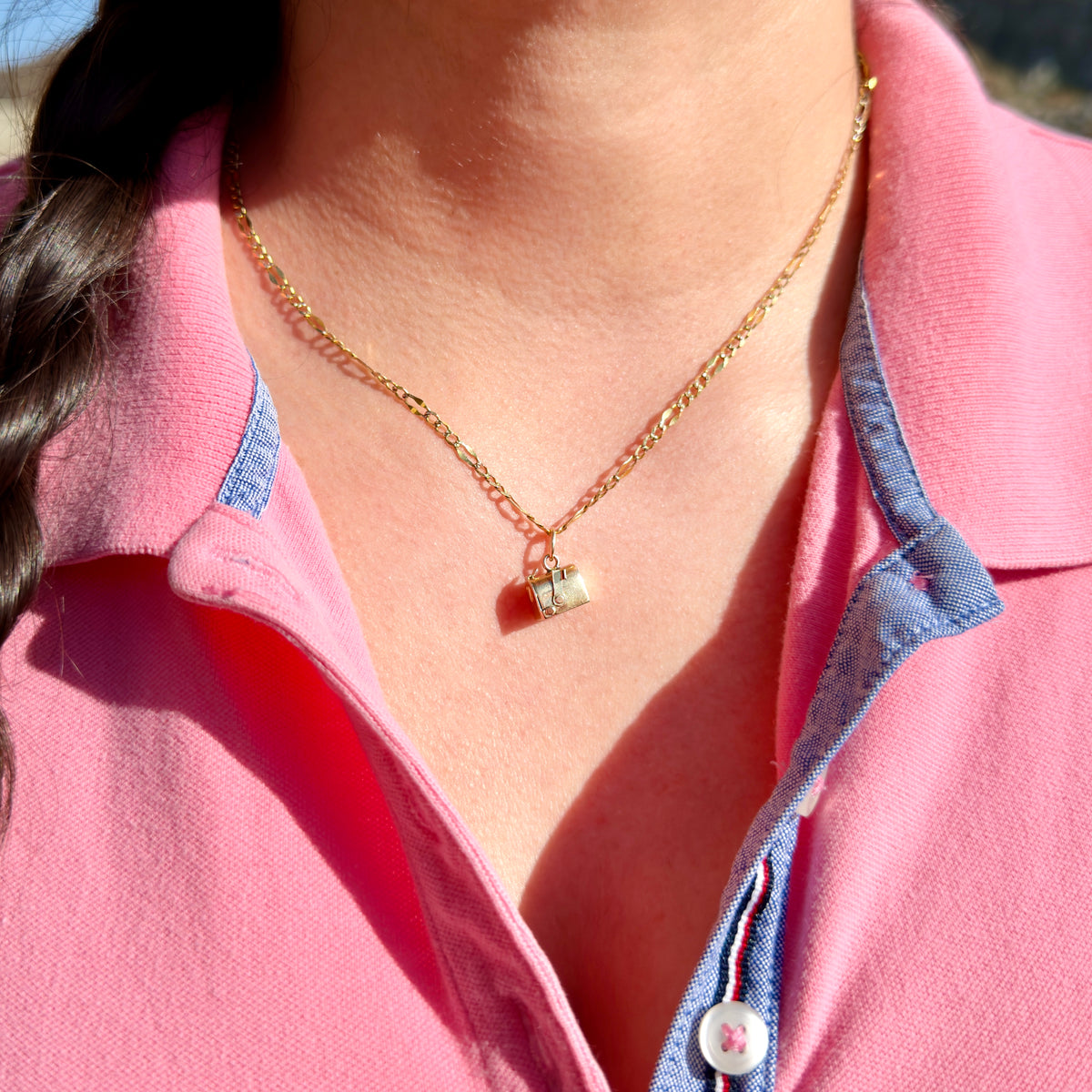 A close-up of a person wearing a delicate gold chain with a small mailbox charm, styled with a pink polo shirt.