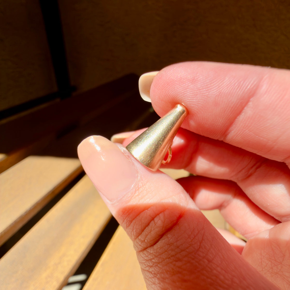 A close-up of a hand holding a megaphone charm against a warm, blurred background.
