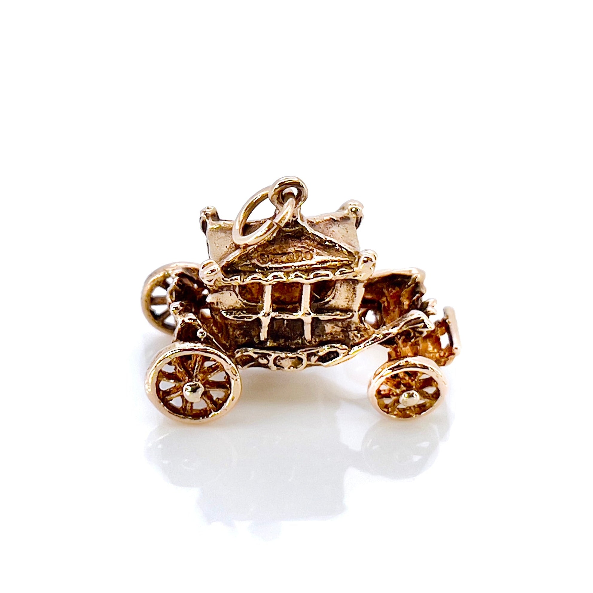 A vintage 9KT gold charm shaped like a Cinderella carriage with moving wheels, crafted in 1962, top view.