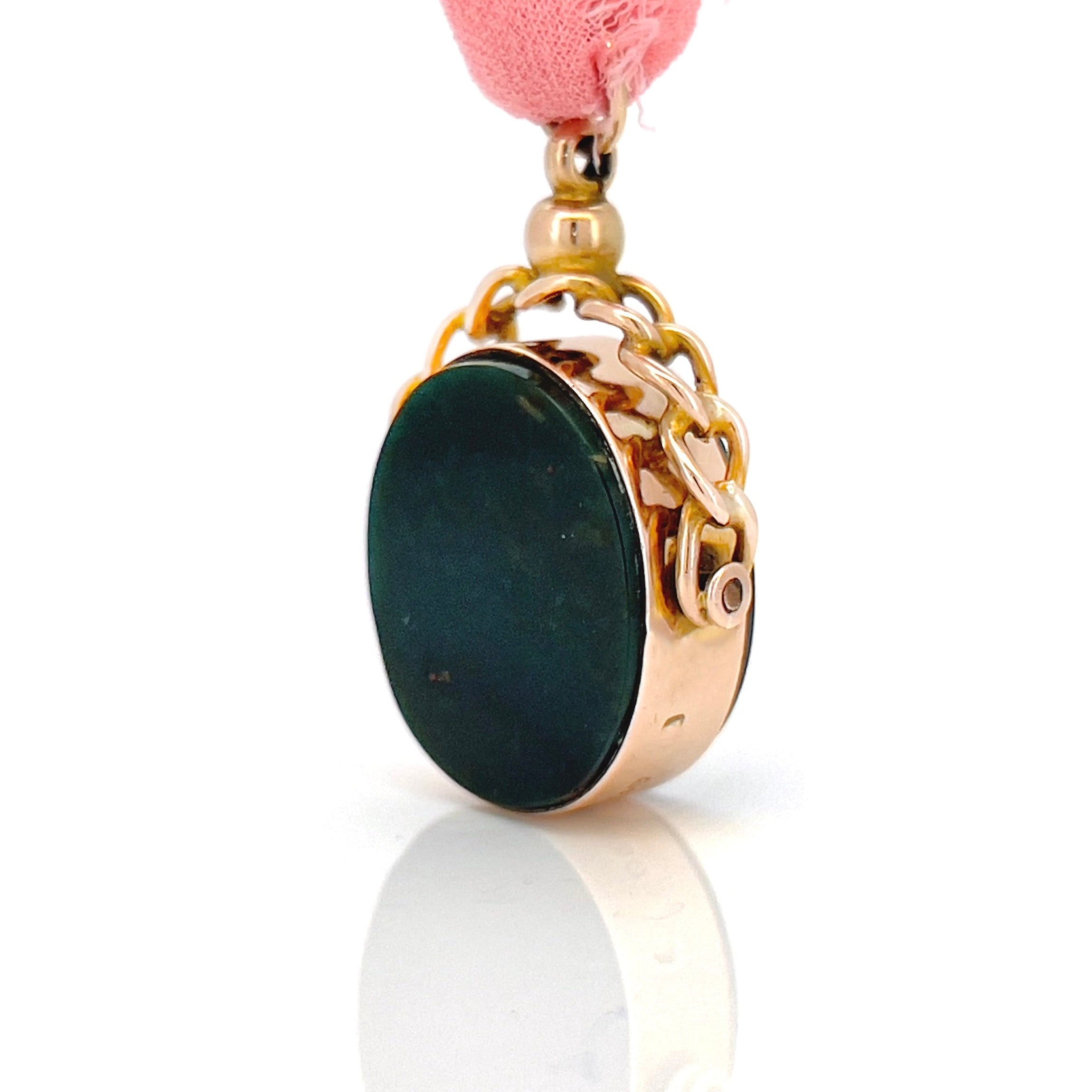 Bloodstone spinning fob with a gold frame hanging from a pink ribbon against a white background.