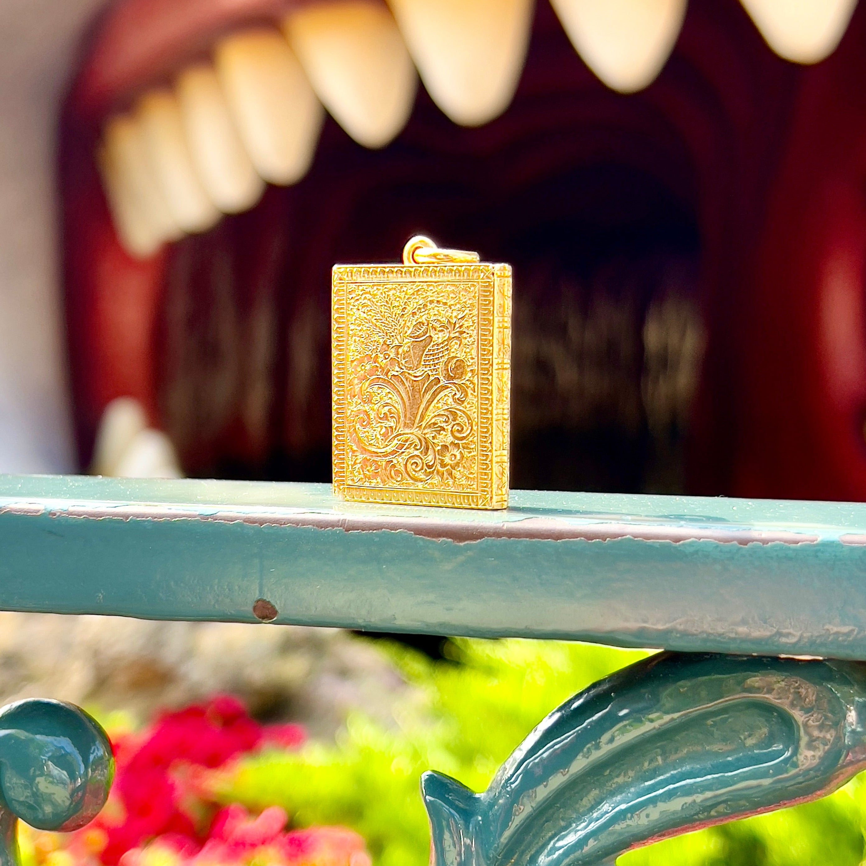Gold book locket on a blue metal surface with a mouth and teeth in the background
