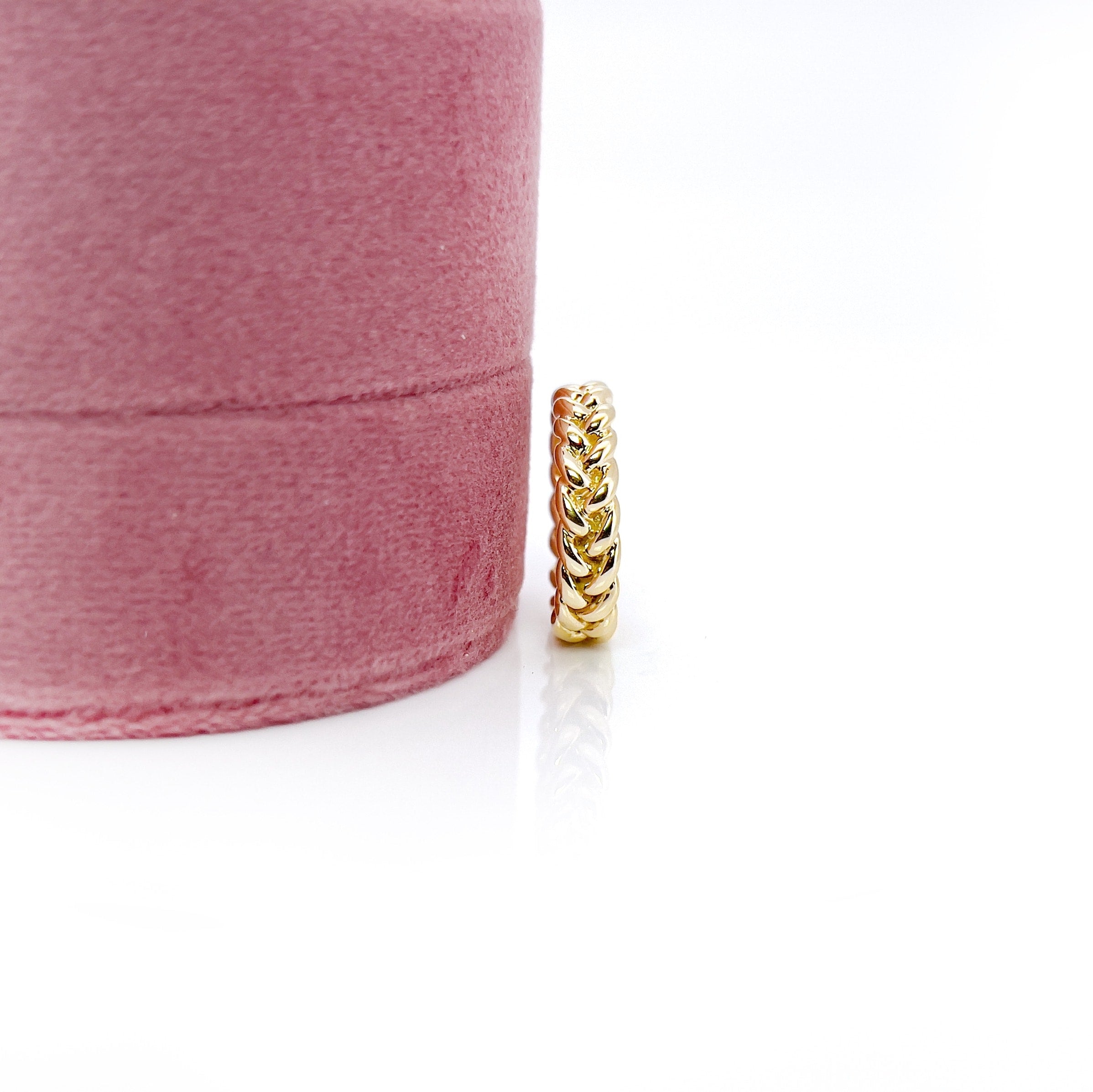 Braided gold vintage ring next to a pink velvet box, with a white background.