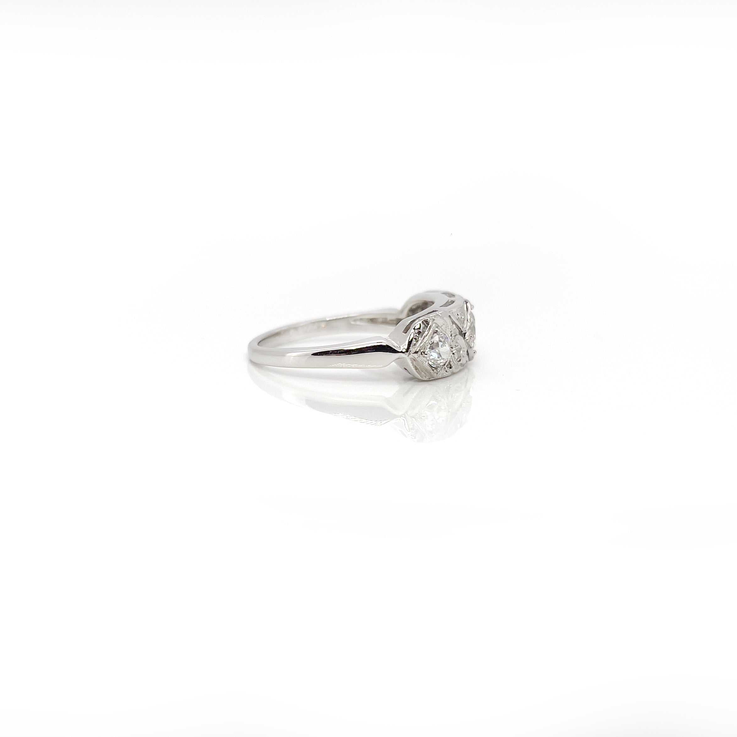 A vintage white gold ring with a central transitional cut diamond flanked by old European cut diamonds, with intricate engraving.