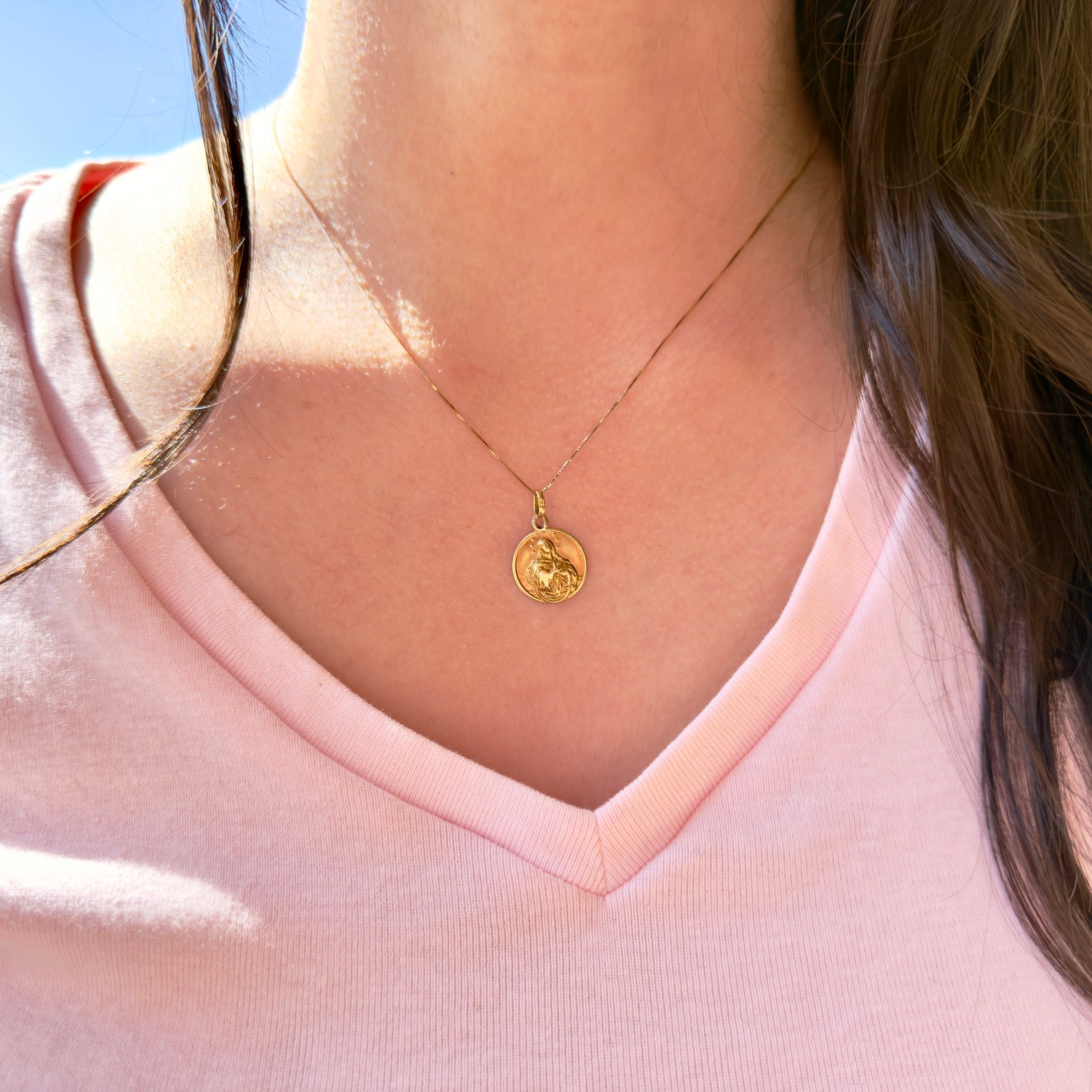 Person wearing a gold necklace with a pendant against a clear blue sky.