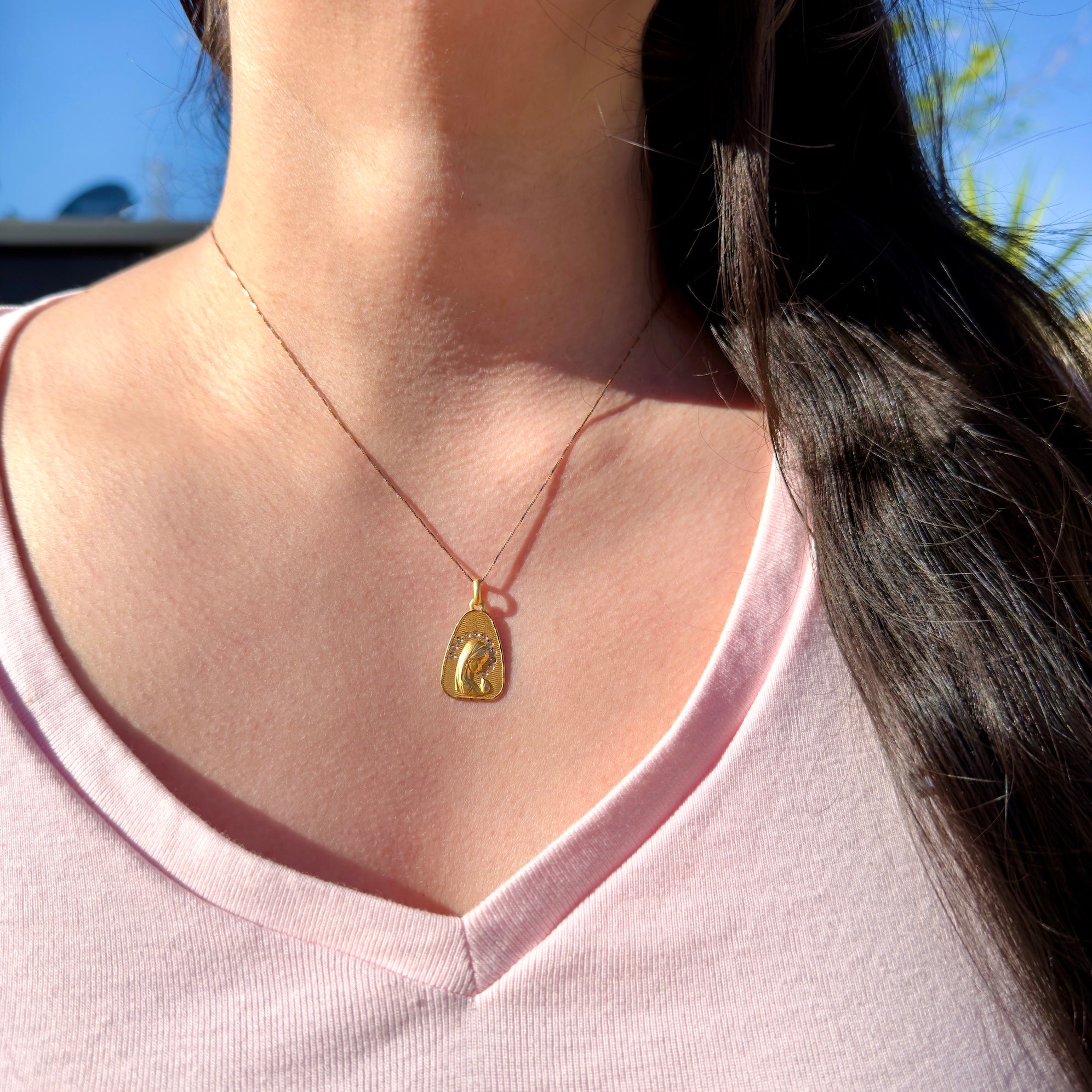 Person wearing a gold necklace with a pendant outdoors