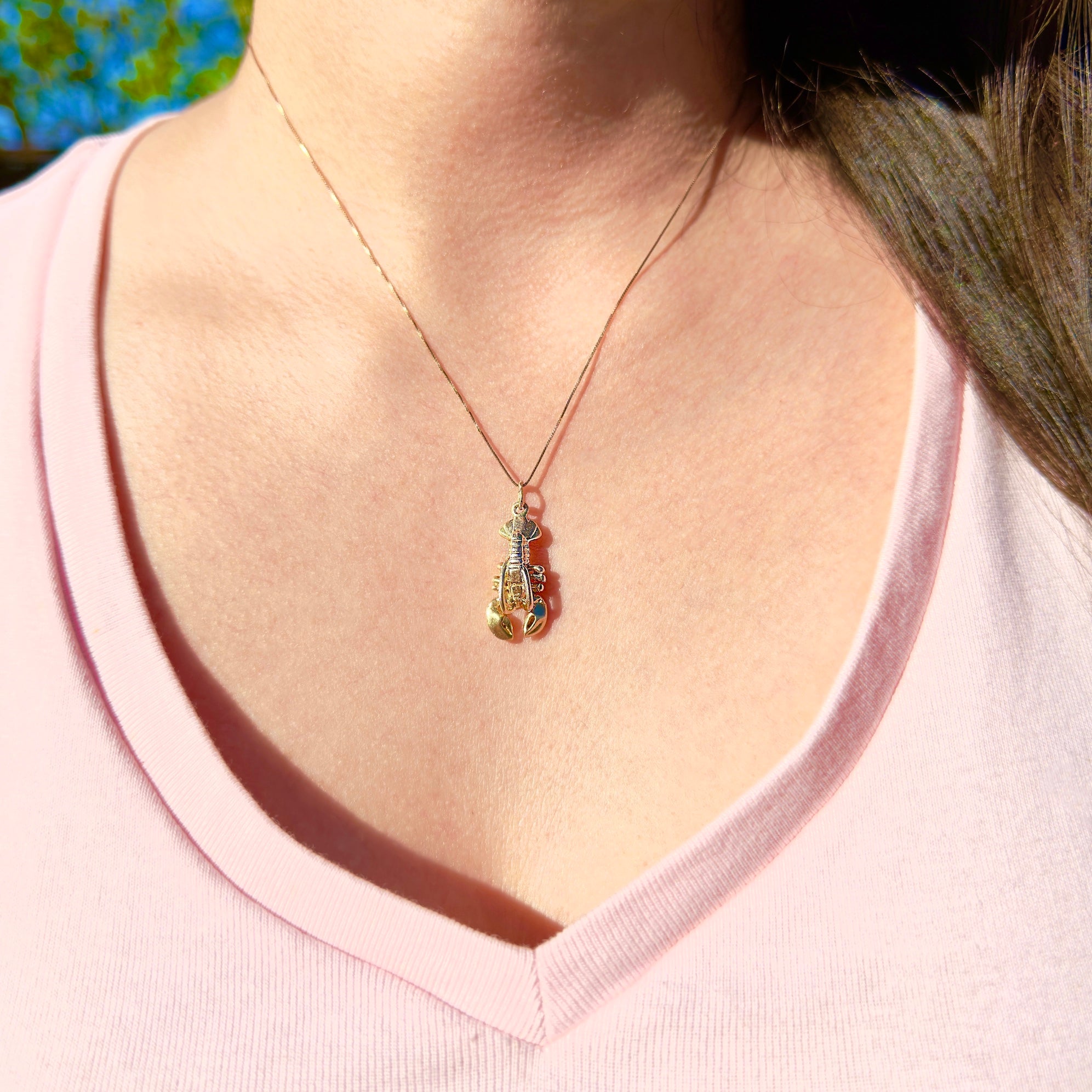 Necklace with a pendant worn by a person in a pink shirt against a blurred natural background