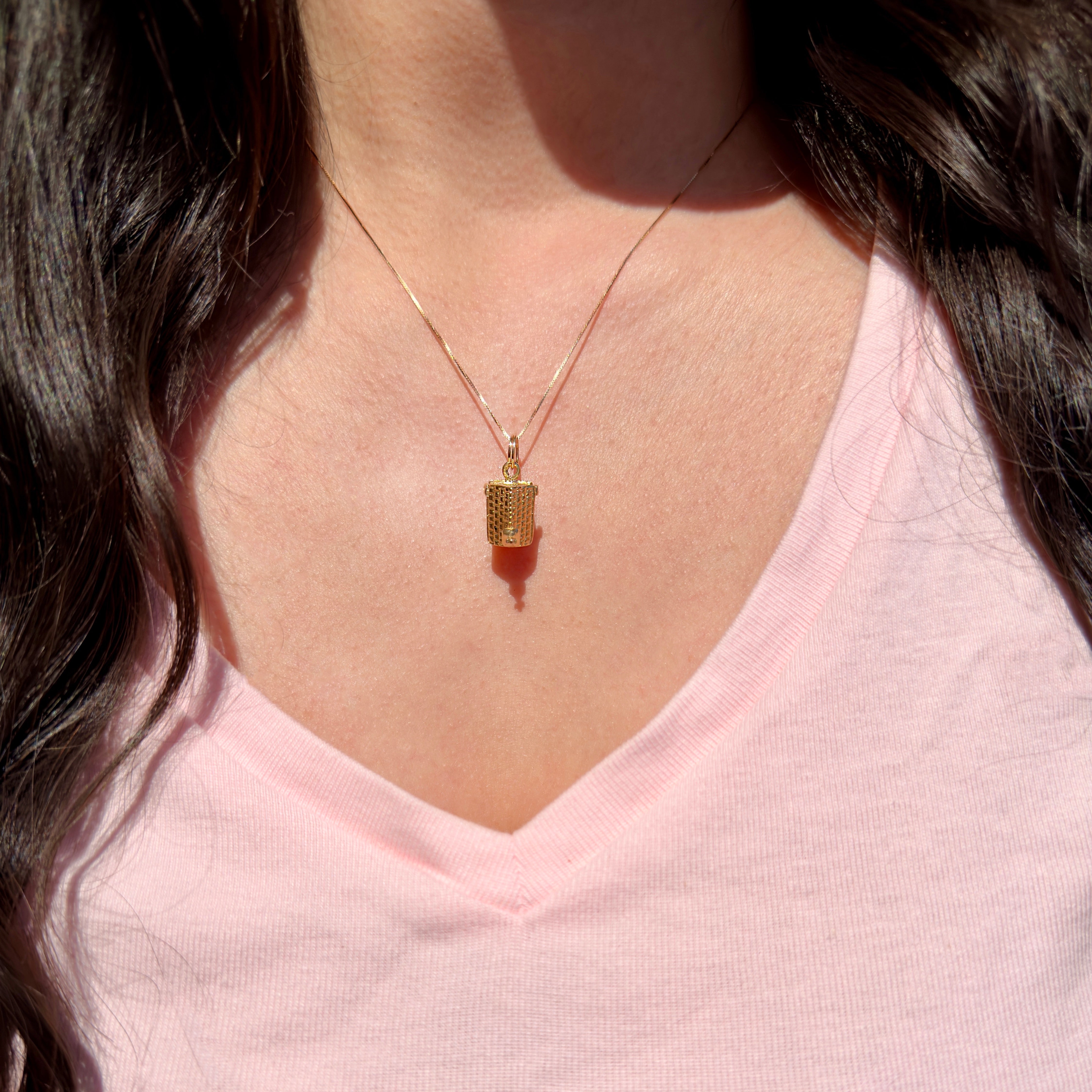 Necklace with a gold pendant worn by a person in a pink shirt.