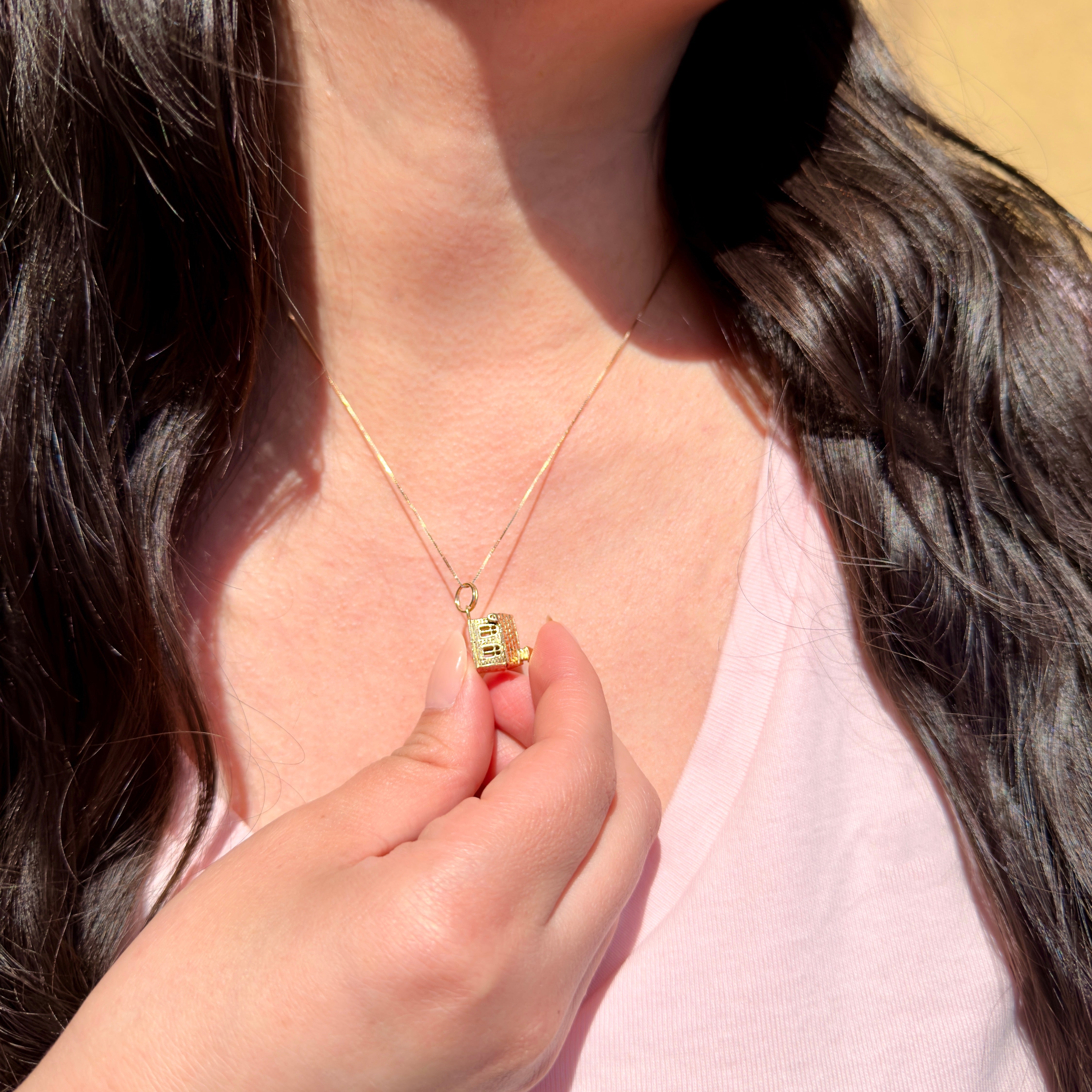 Person wearing a gold necklace with a vintage gold church charm.