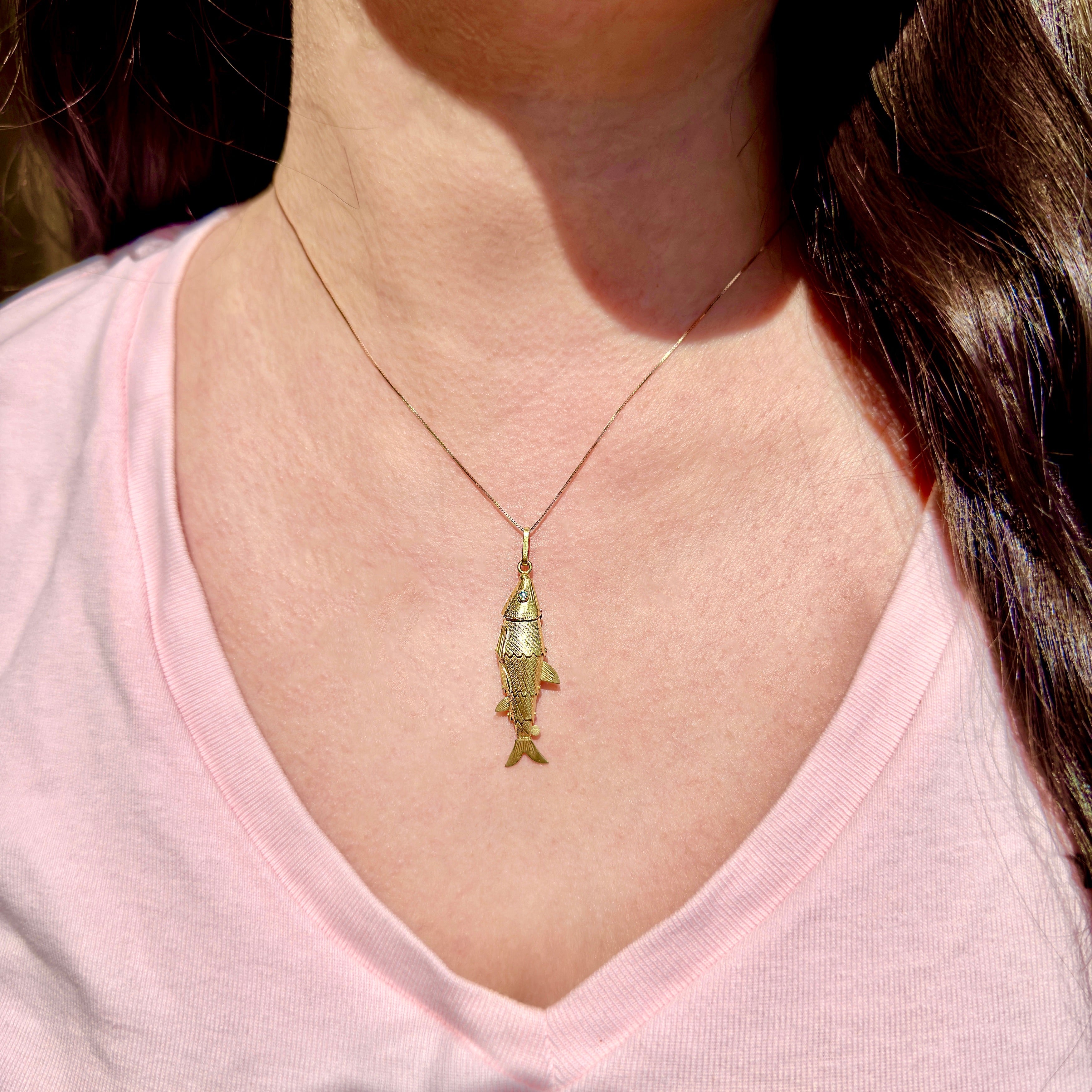 Person wearing a gold fish pendant necklace on a pink shirt