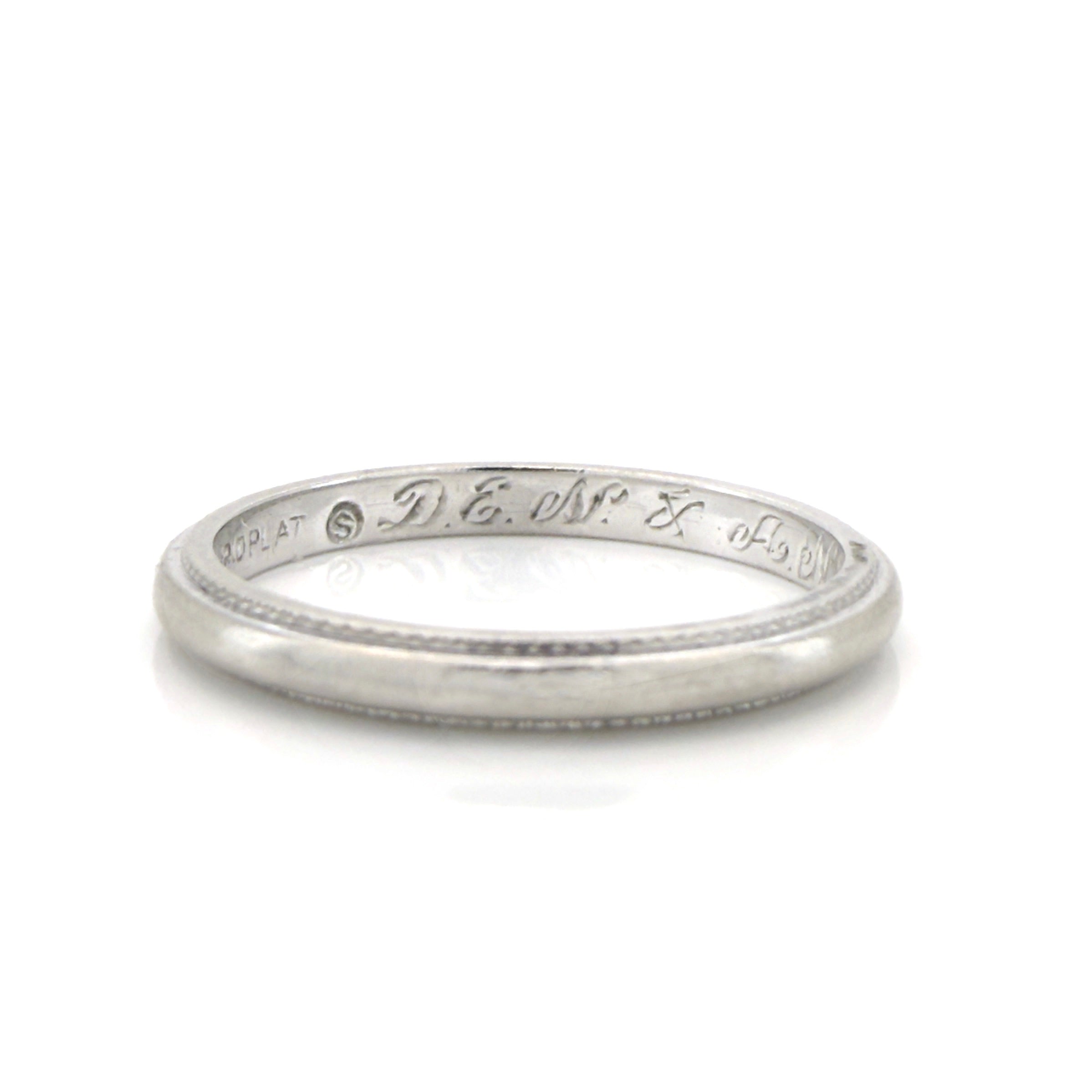 Vintage platinum ring with engraved text on a white background
