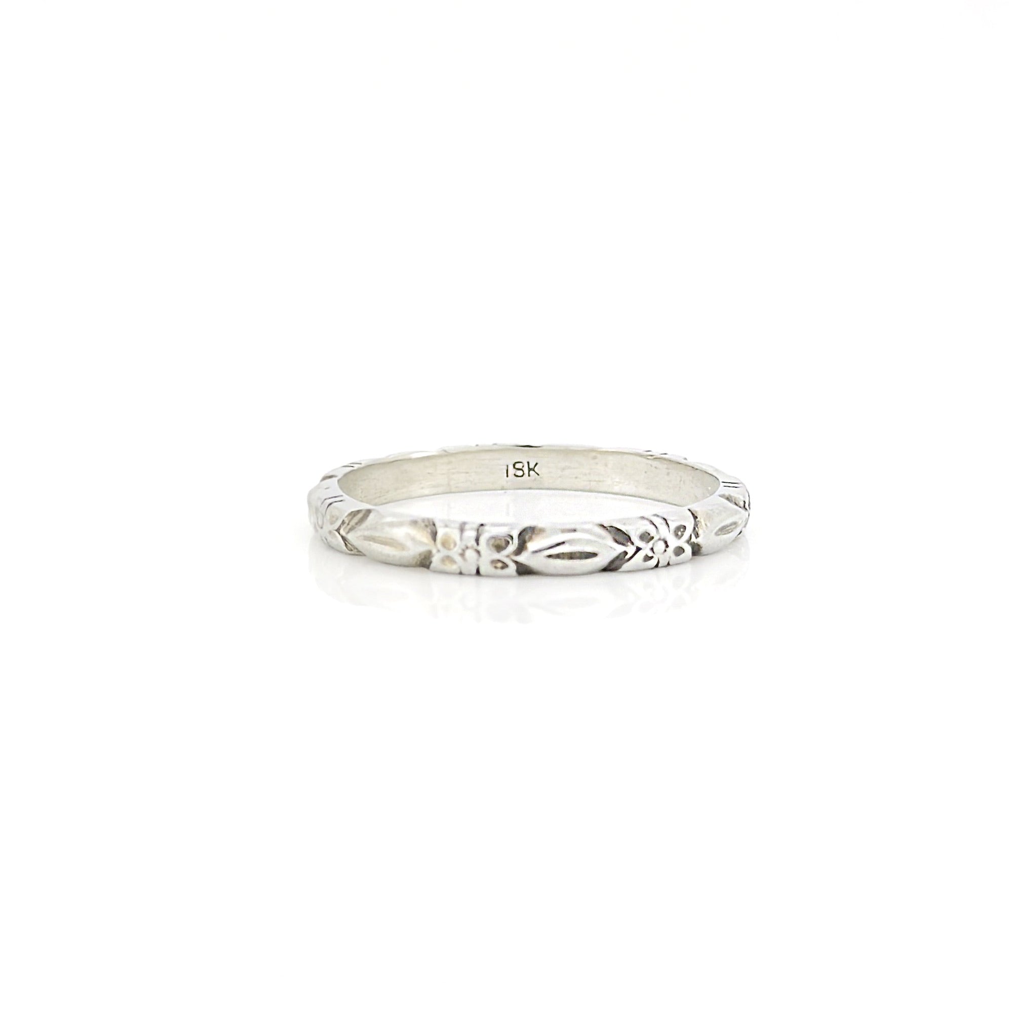 White gold ring with a flower pattern and an '18K' stamp on a white background