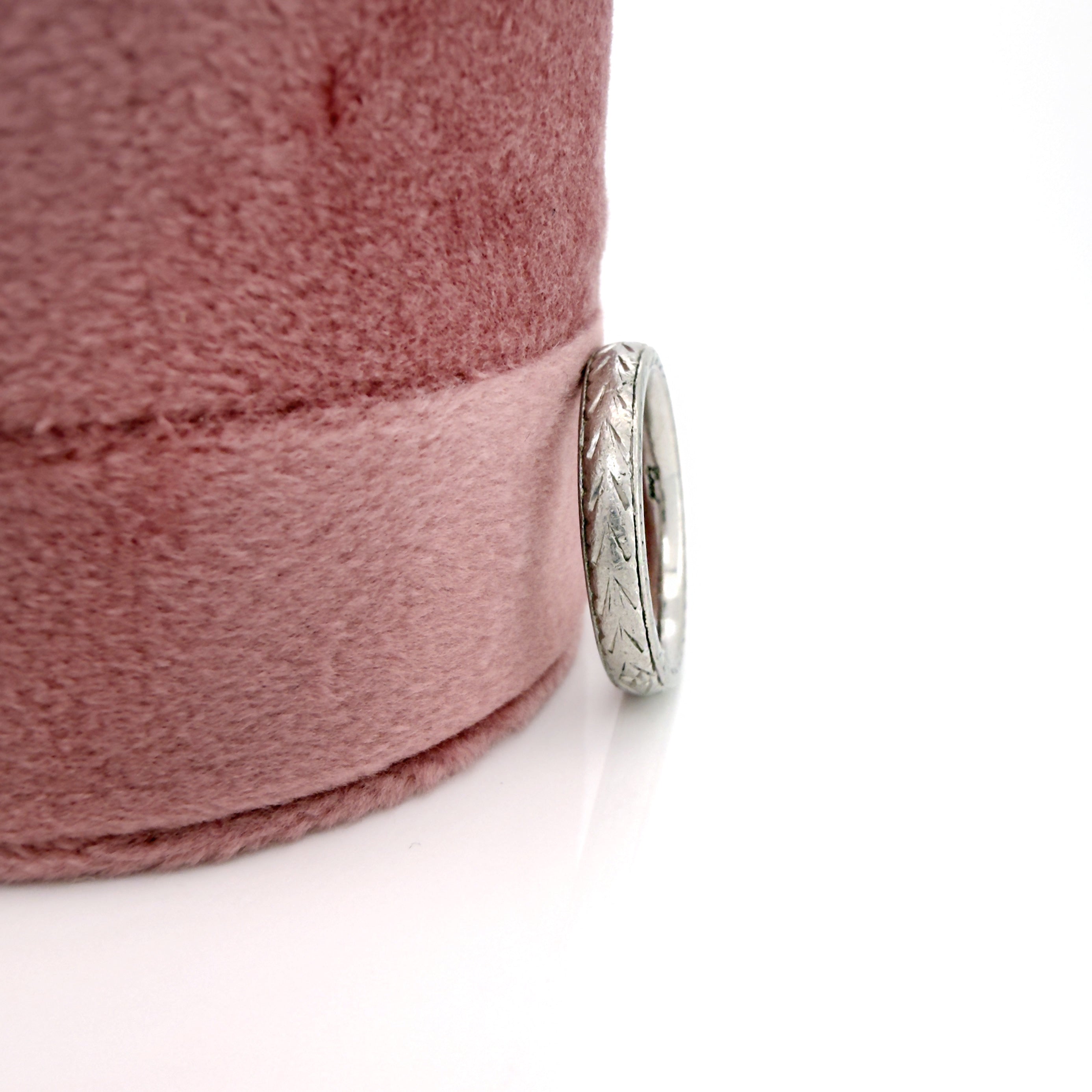 Vintage platinum ring with intricate design against a pink fabric ring box against a white background