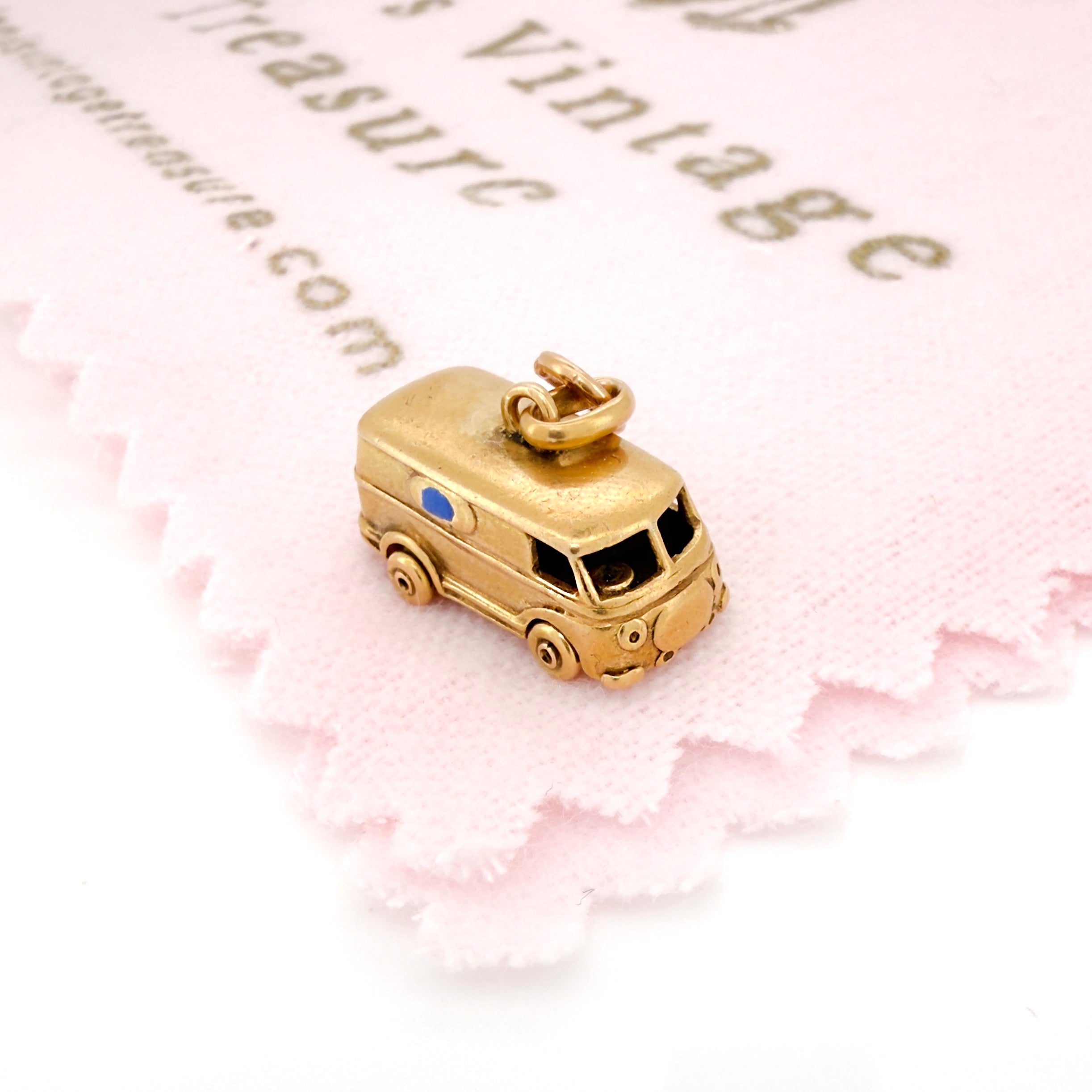 Vintage gold microbus  charm with a light blue enamel window on a pink and white background