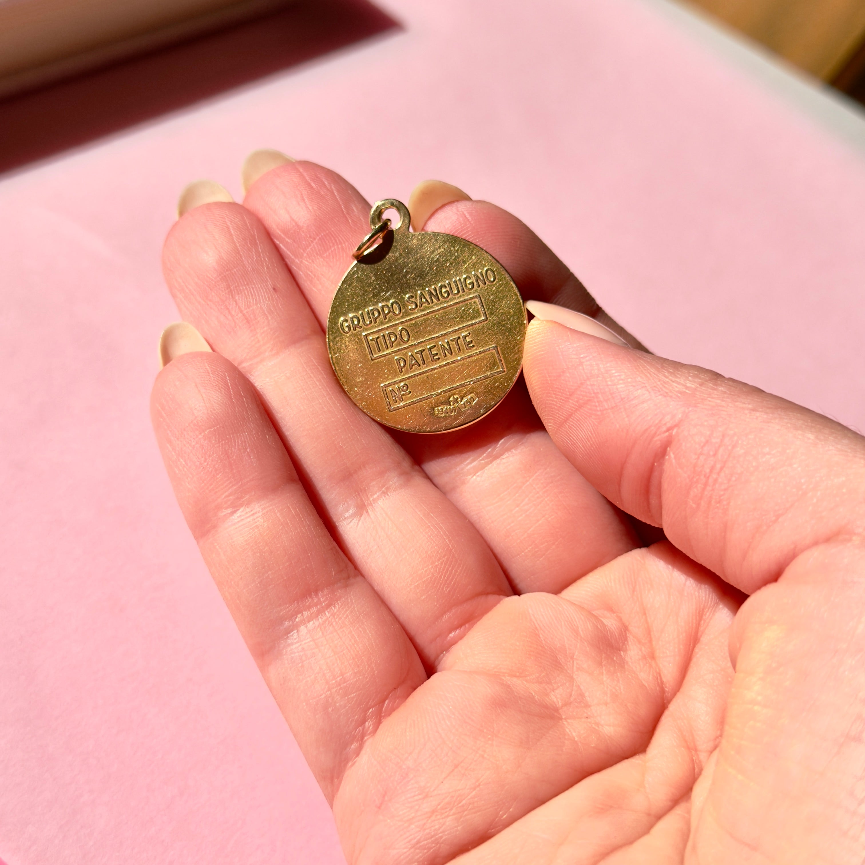 Vintage gold pendant held in a hand against a pink background