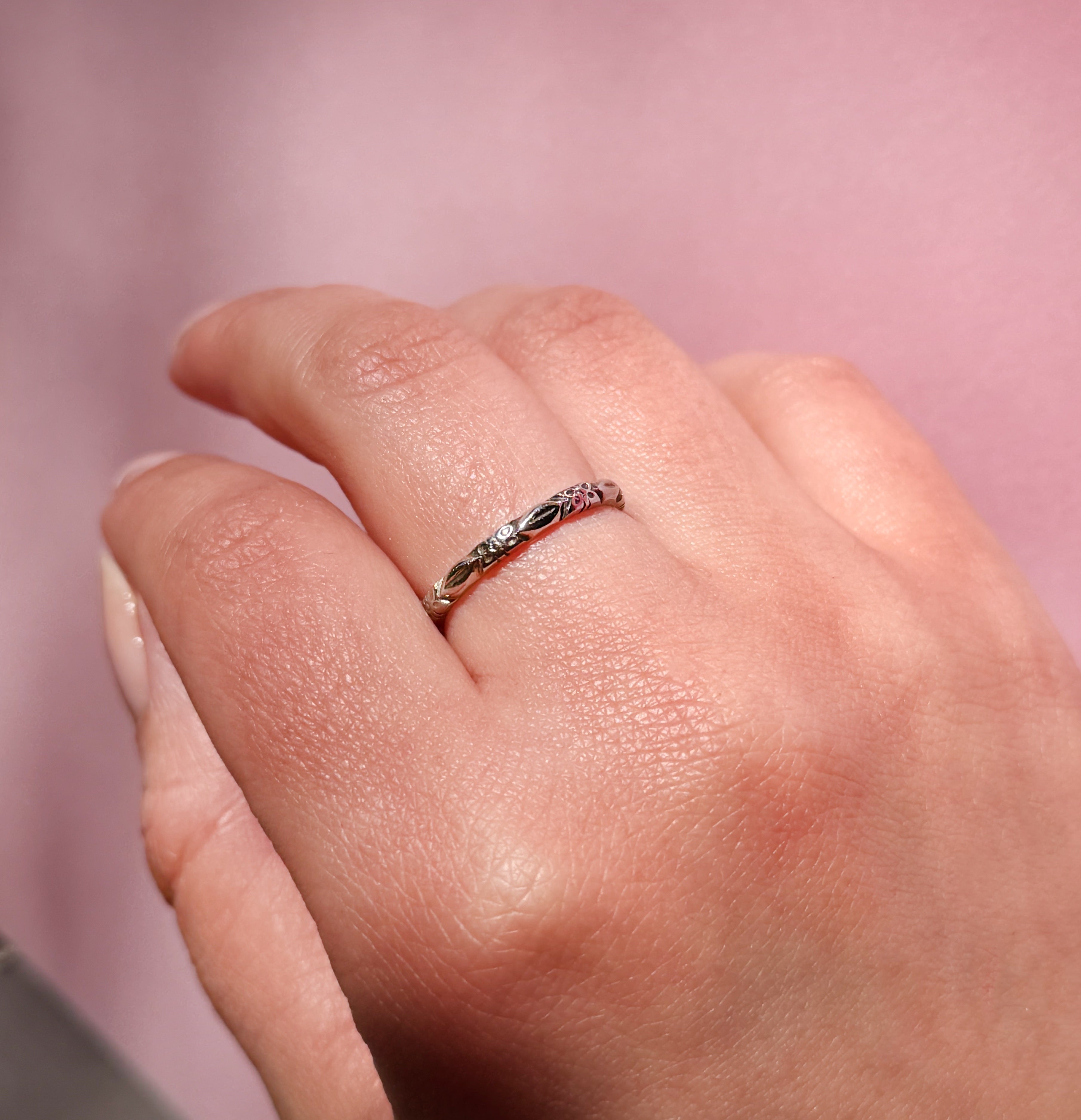 Hand wearing a white gold ring with a flower pattern on a pink background