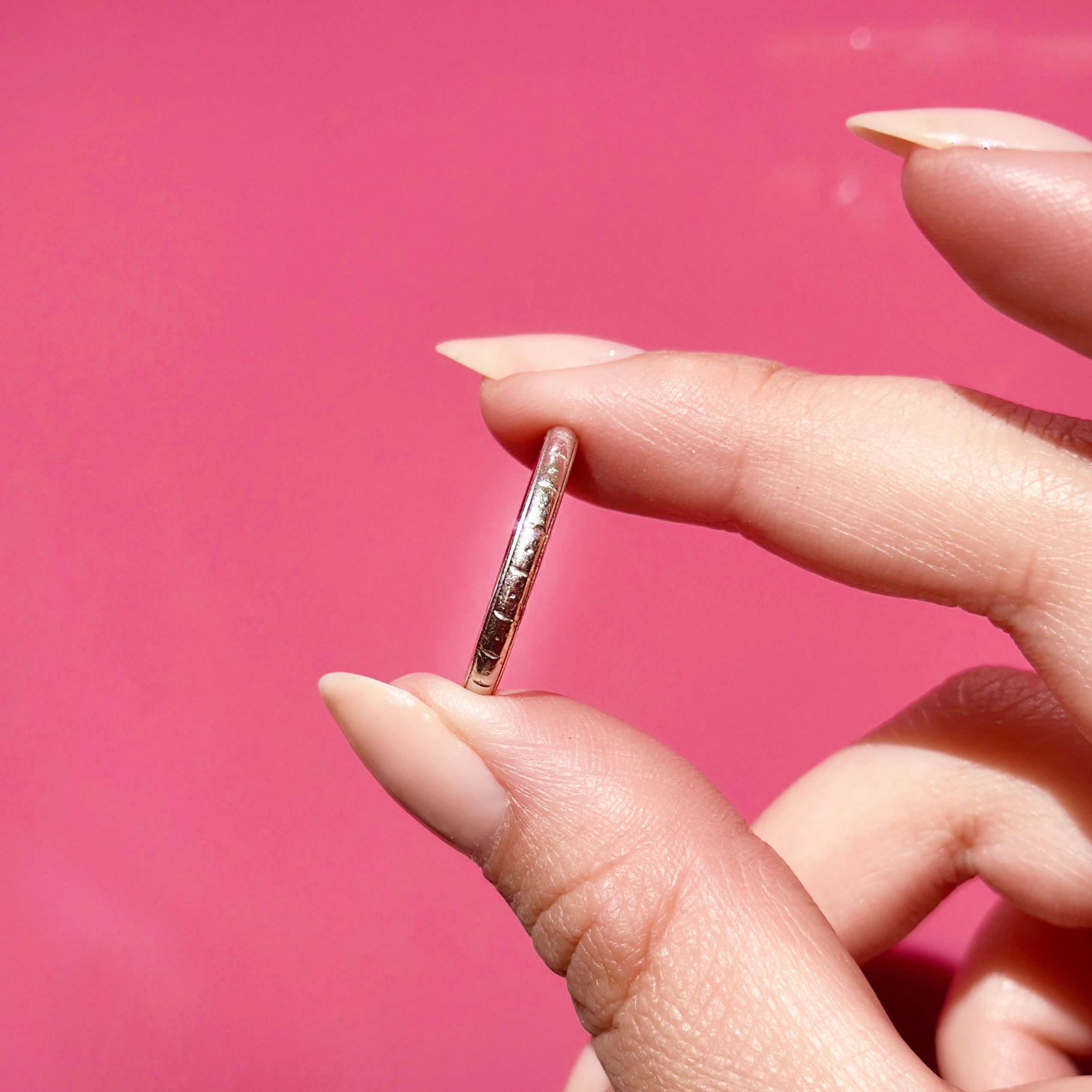 Platinum ring held between fingers against a pink background