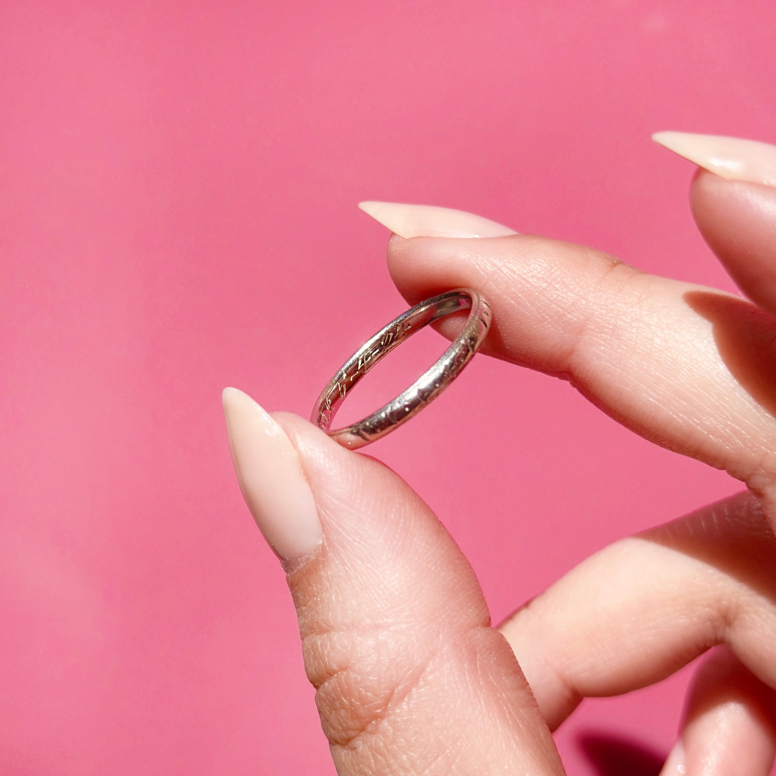 Platinum ring held between fingers against a pink background