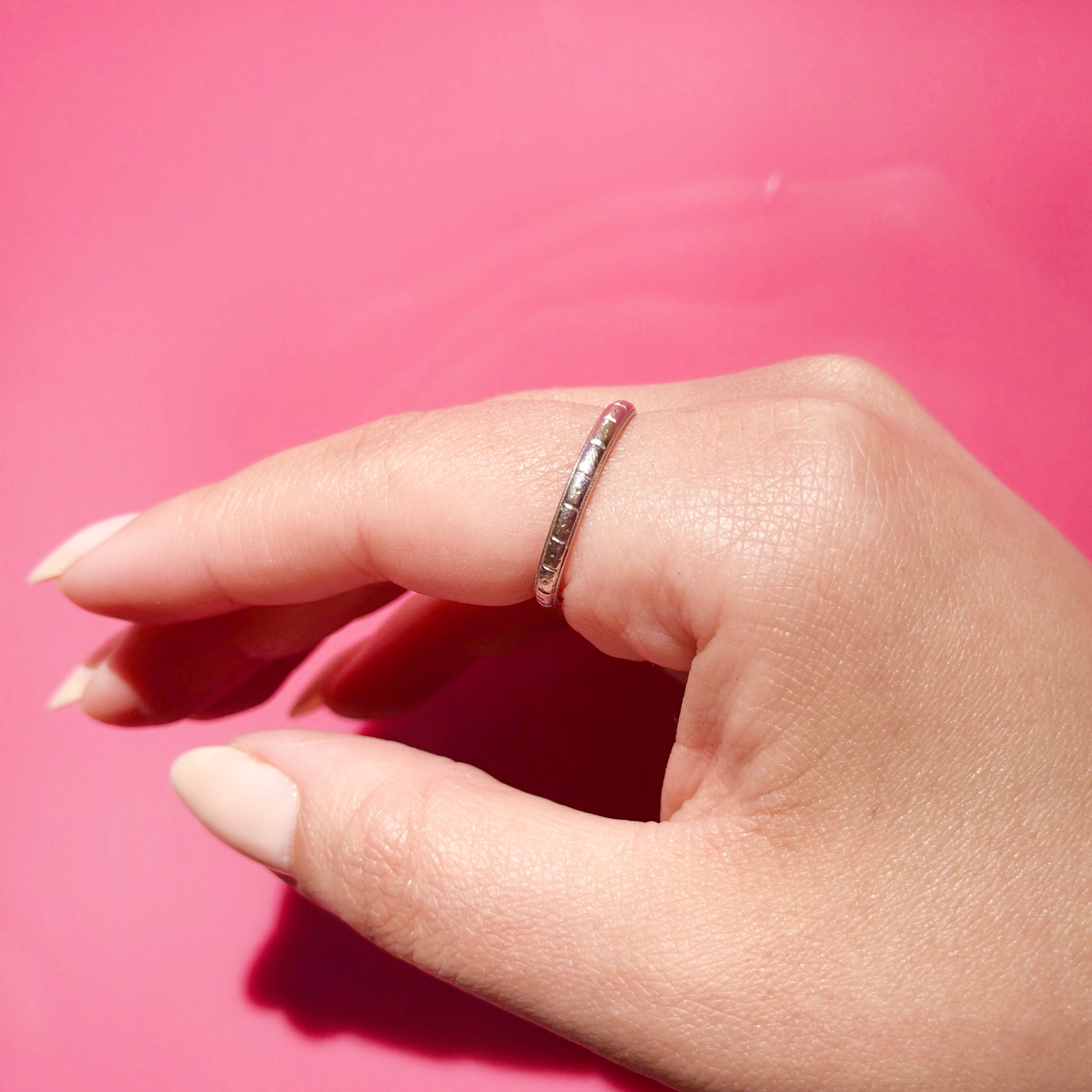 Hand wearing an antique platinum ring on a pink background