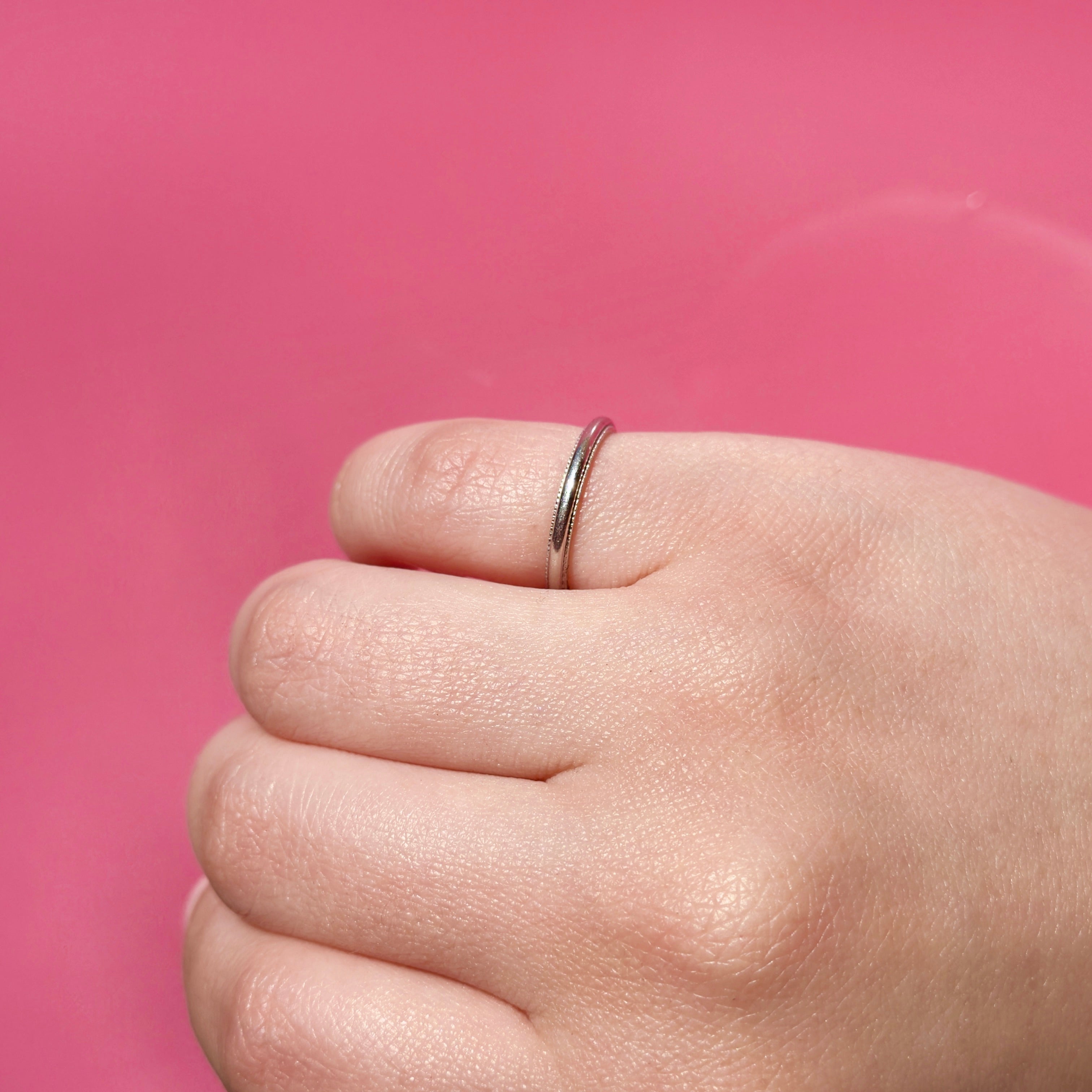 Hand wearing a vintage platinum ring on a pink background
