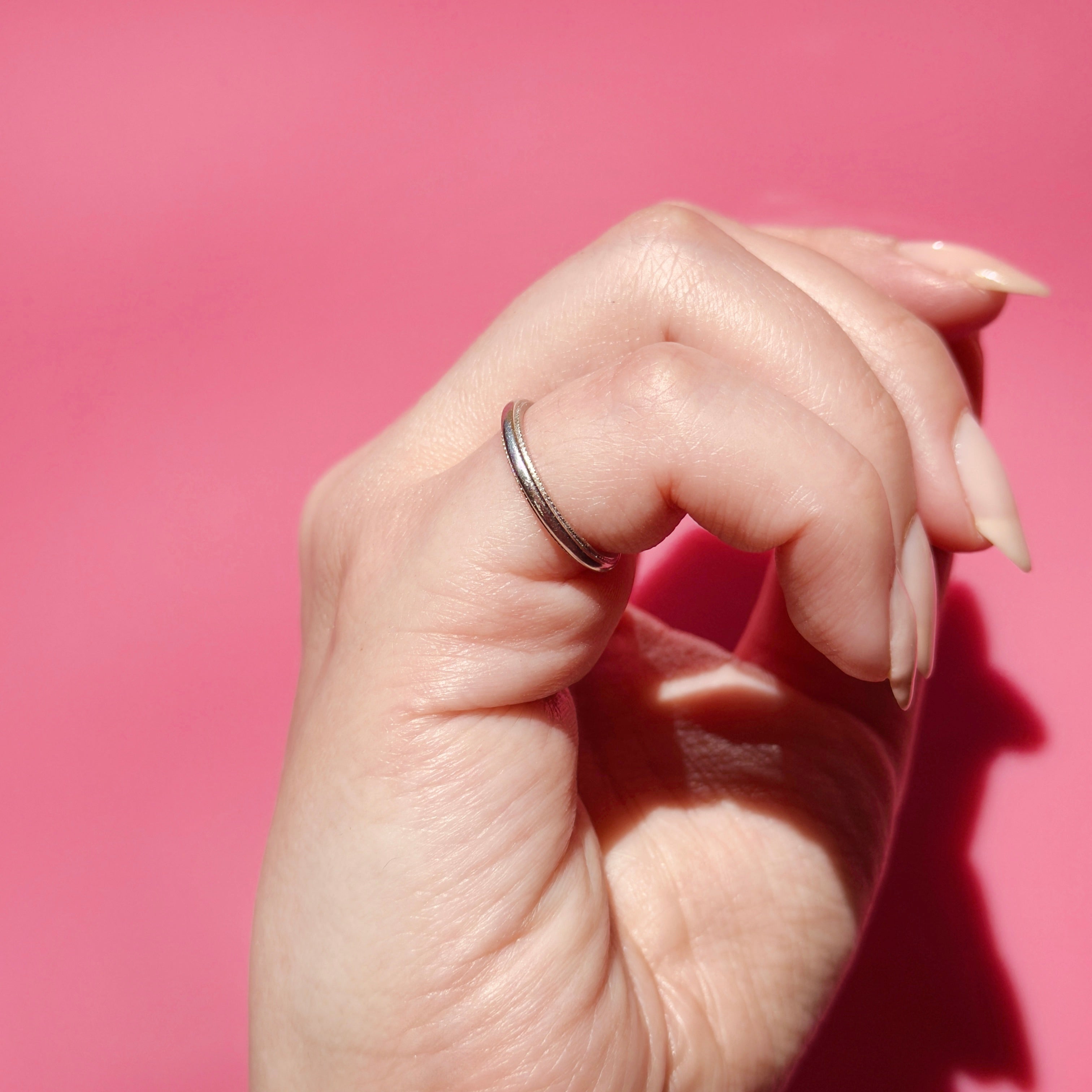 Hand wearing a vintage platinum ring on a pink background