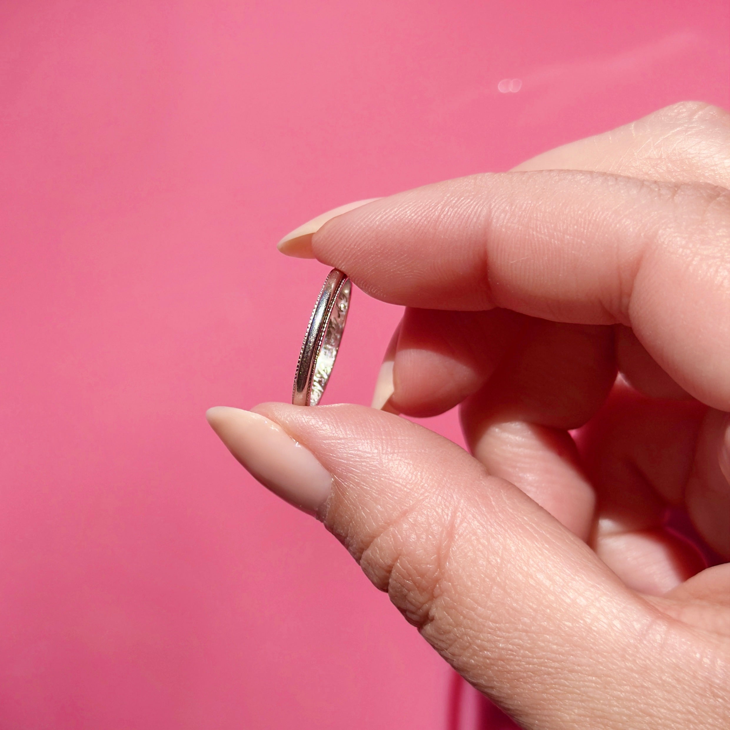 Close-up of a hand holding a vintage platinum ring against a pink background