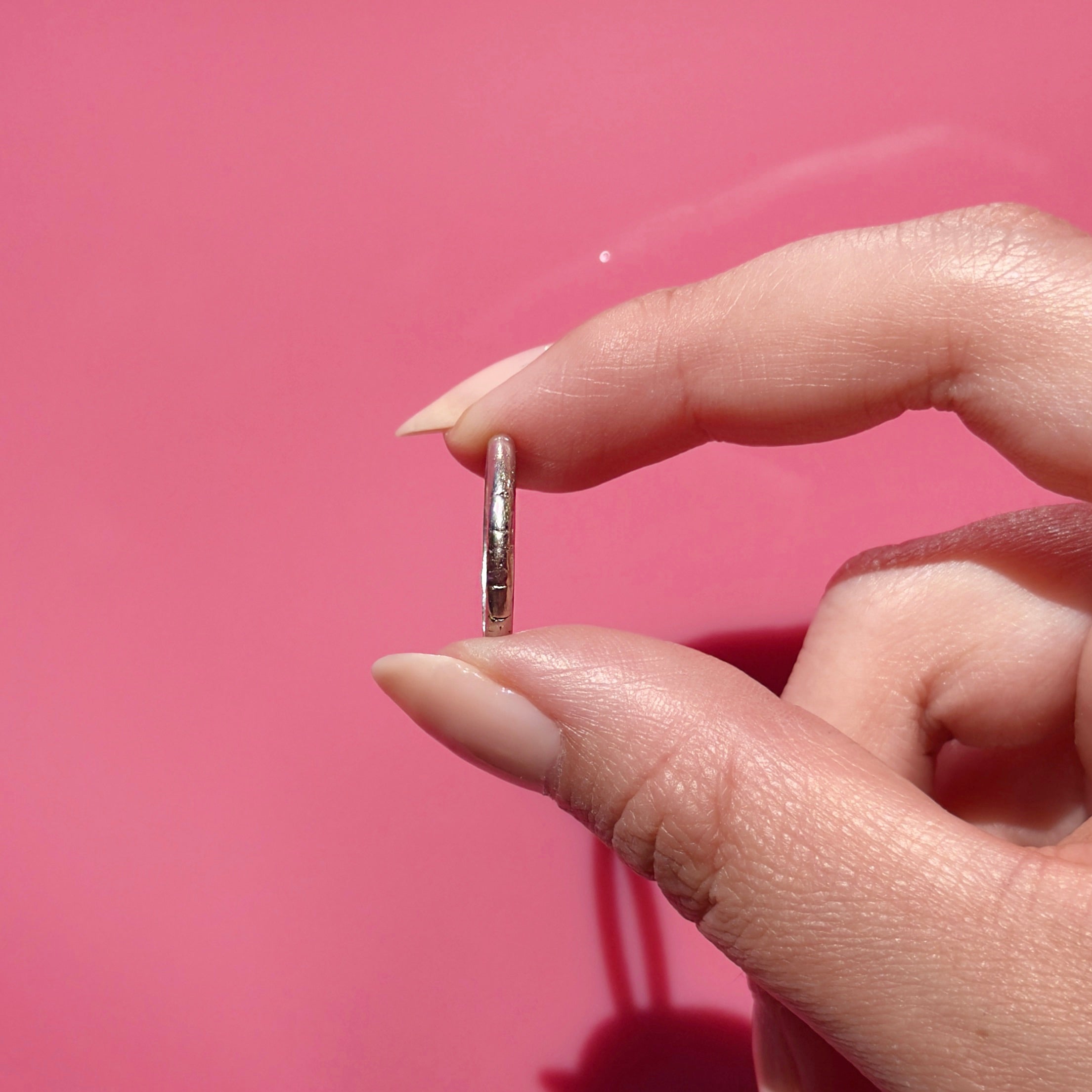 Hand holding an antique platinum ring against a pink background