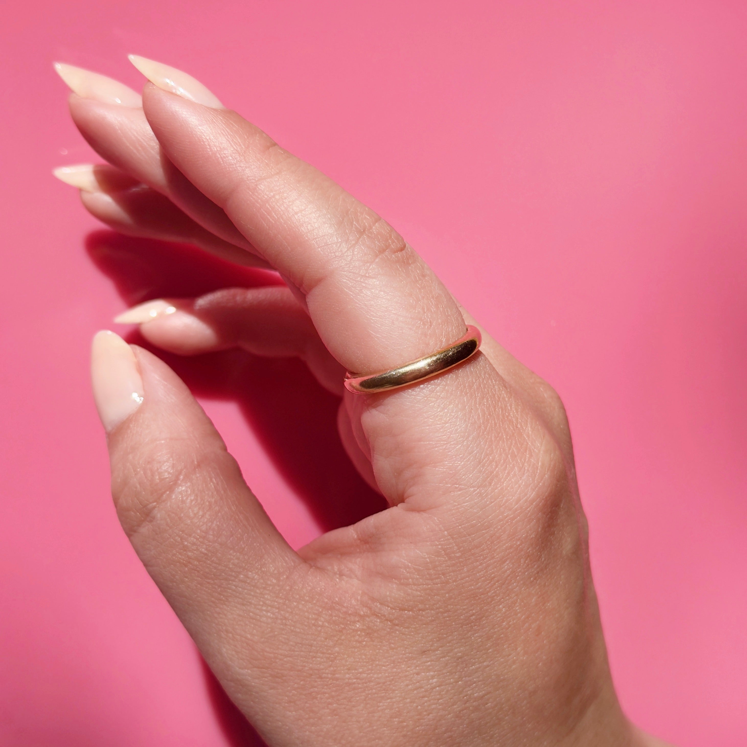 Hand wearing a gold ring with pink background