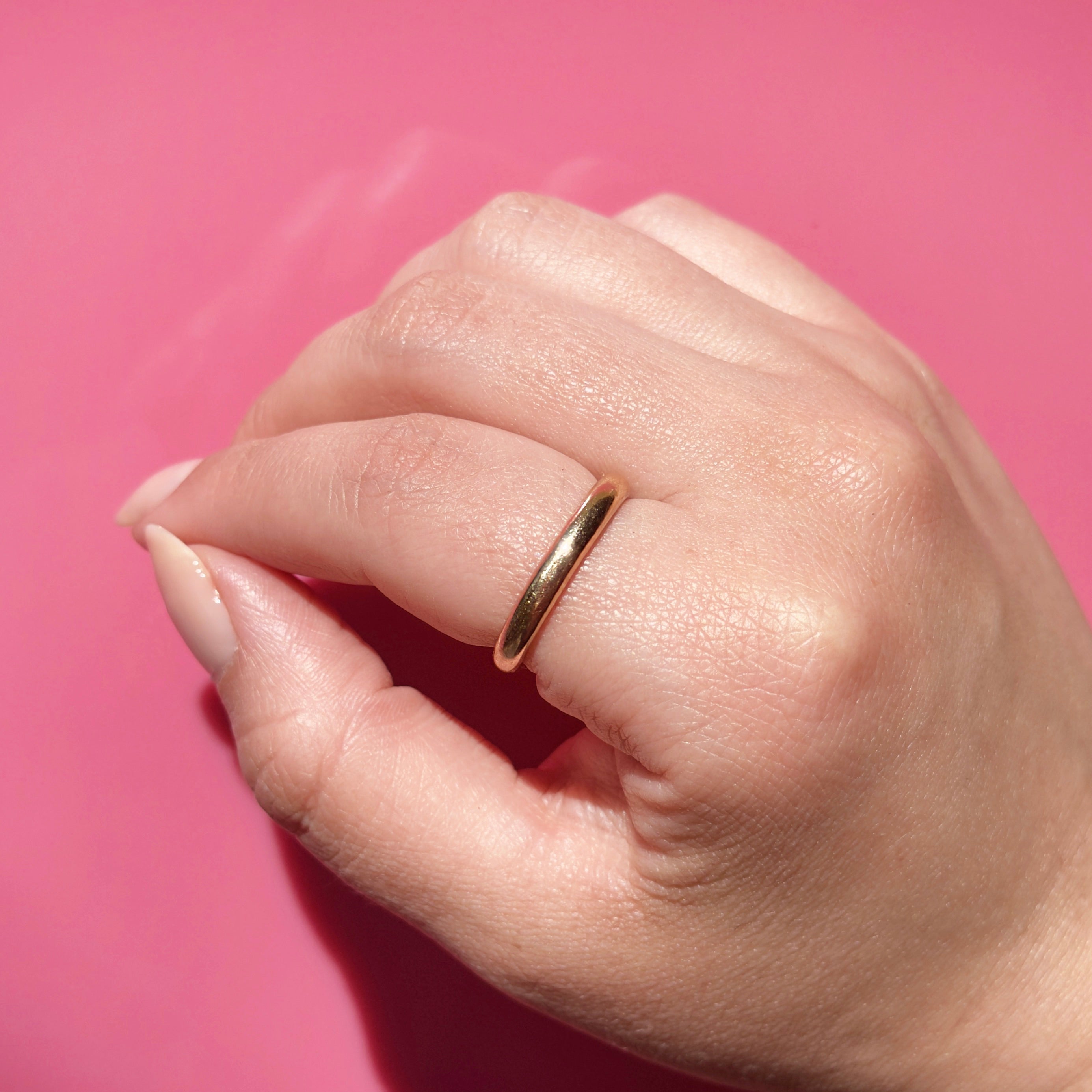 Antique gold ring on a person's finger against a pink background