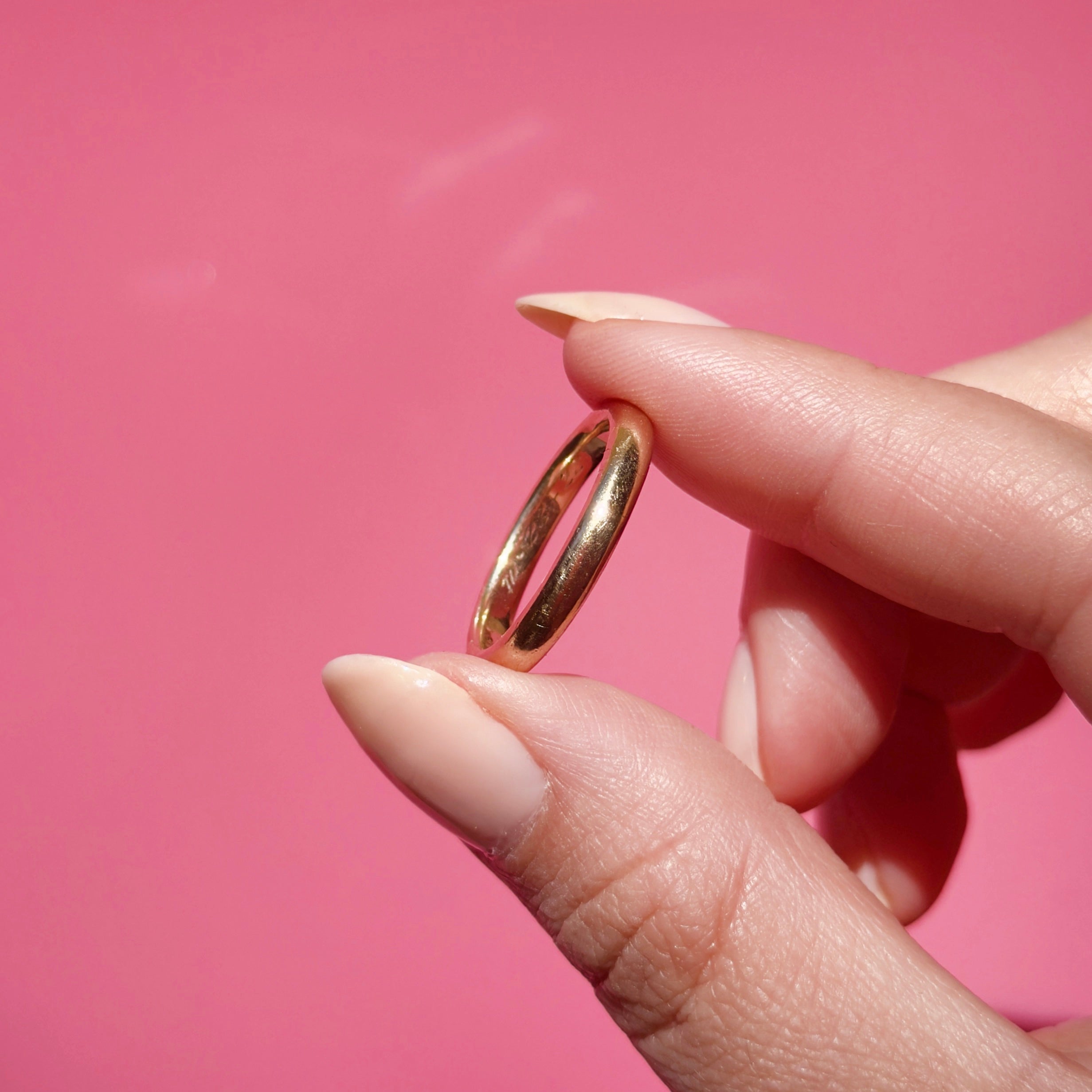 Antique gold ring held between fingers against a pink background