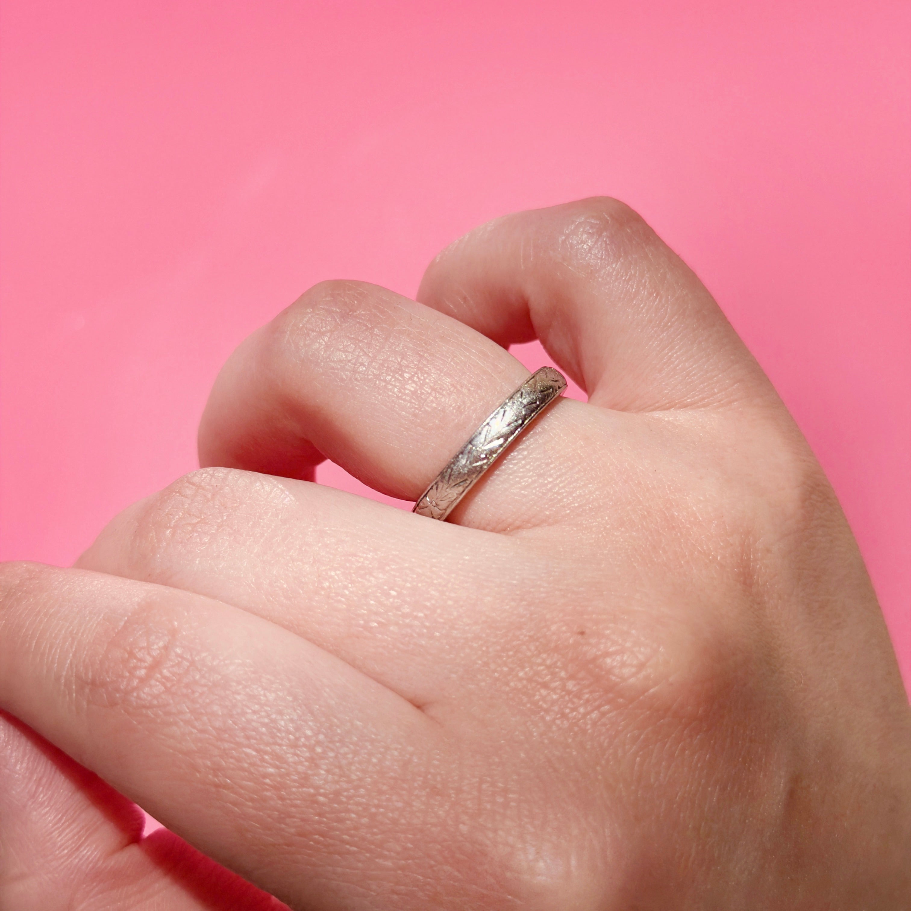 Hand wearing a vintage platinum ring with a pink background