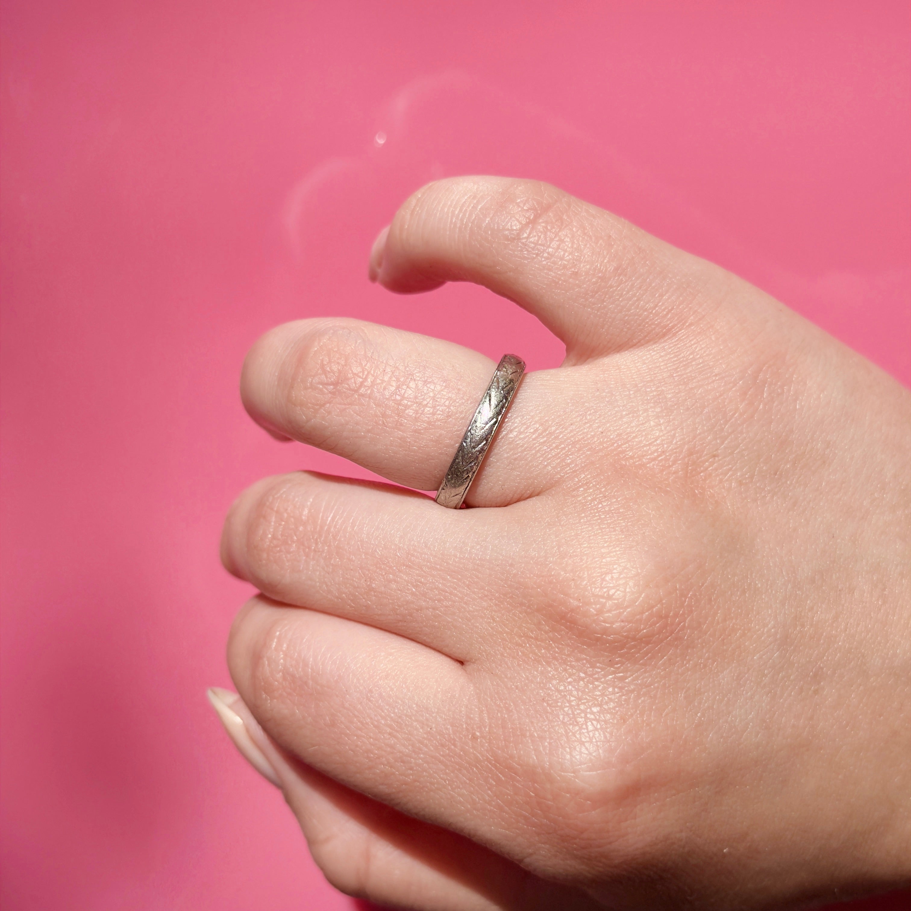 Hand wearing a vintage platinum ring with a pink background