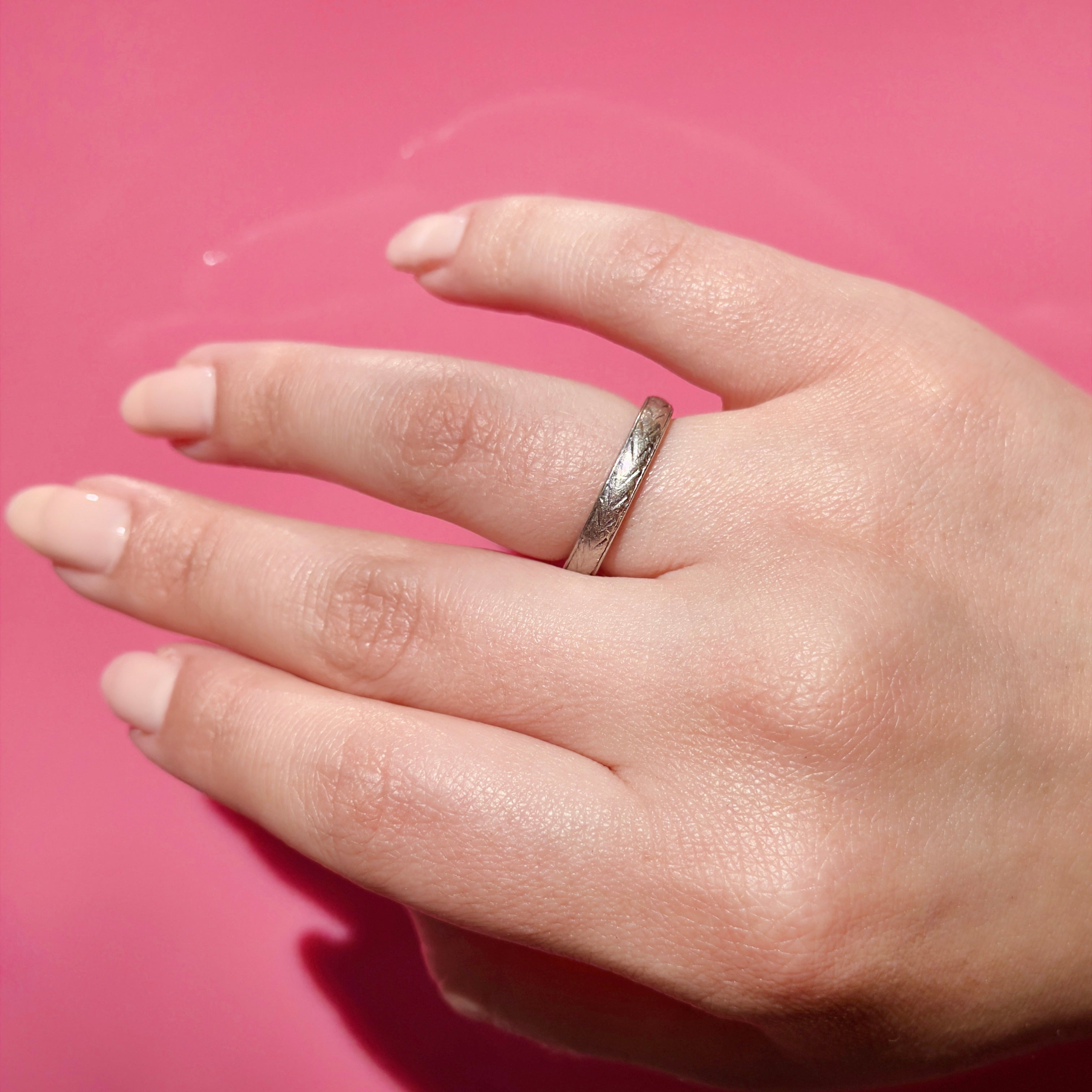 Hand wearing a vintage platinum ring with a pink background