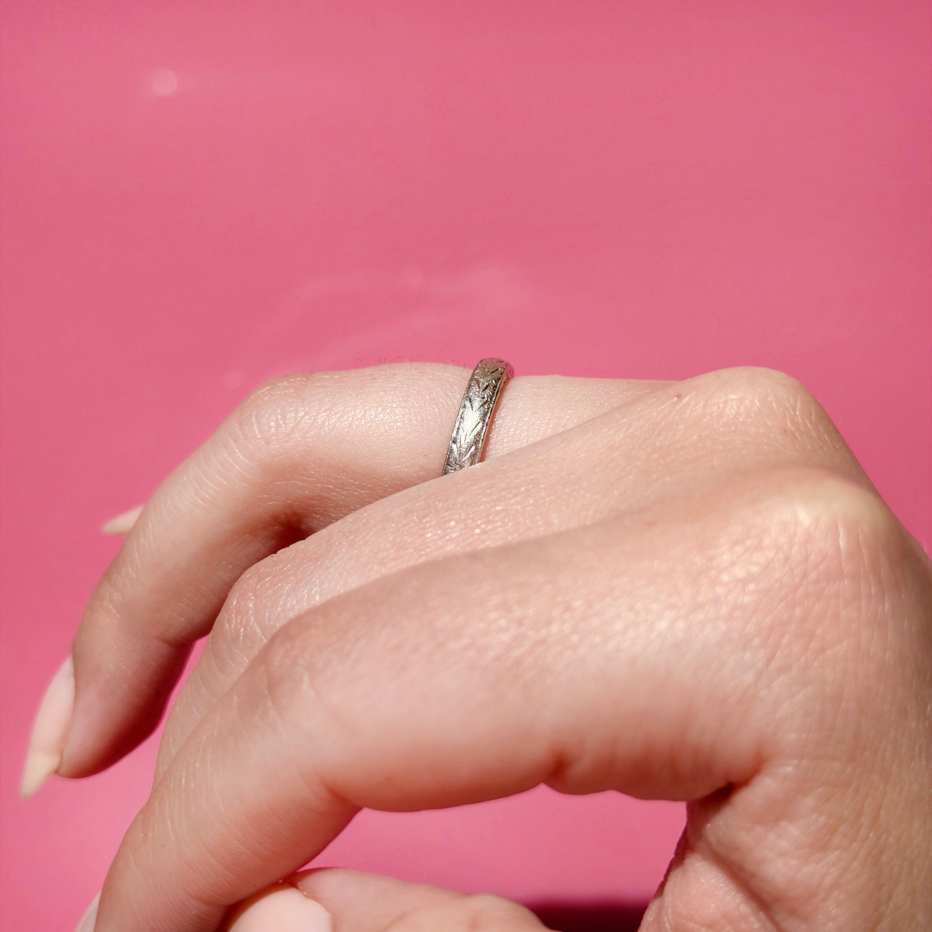 Vintage platinum ring on a finger against a pink background