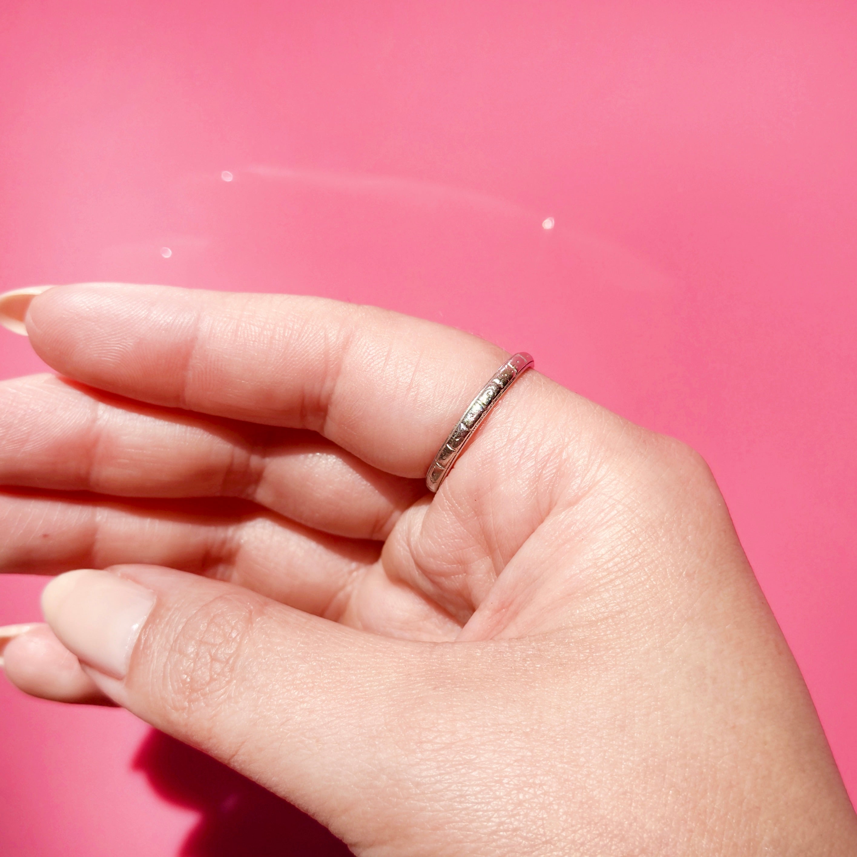 Hand wearing an antique platinum ring on a pink background