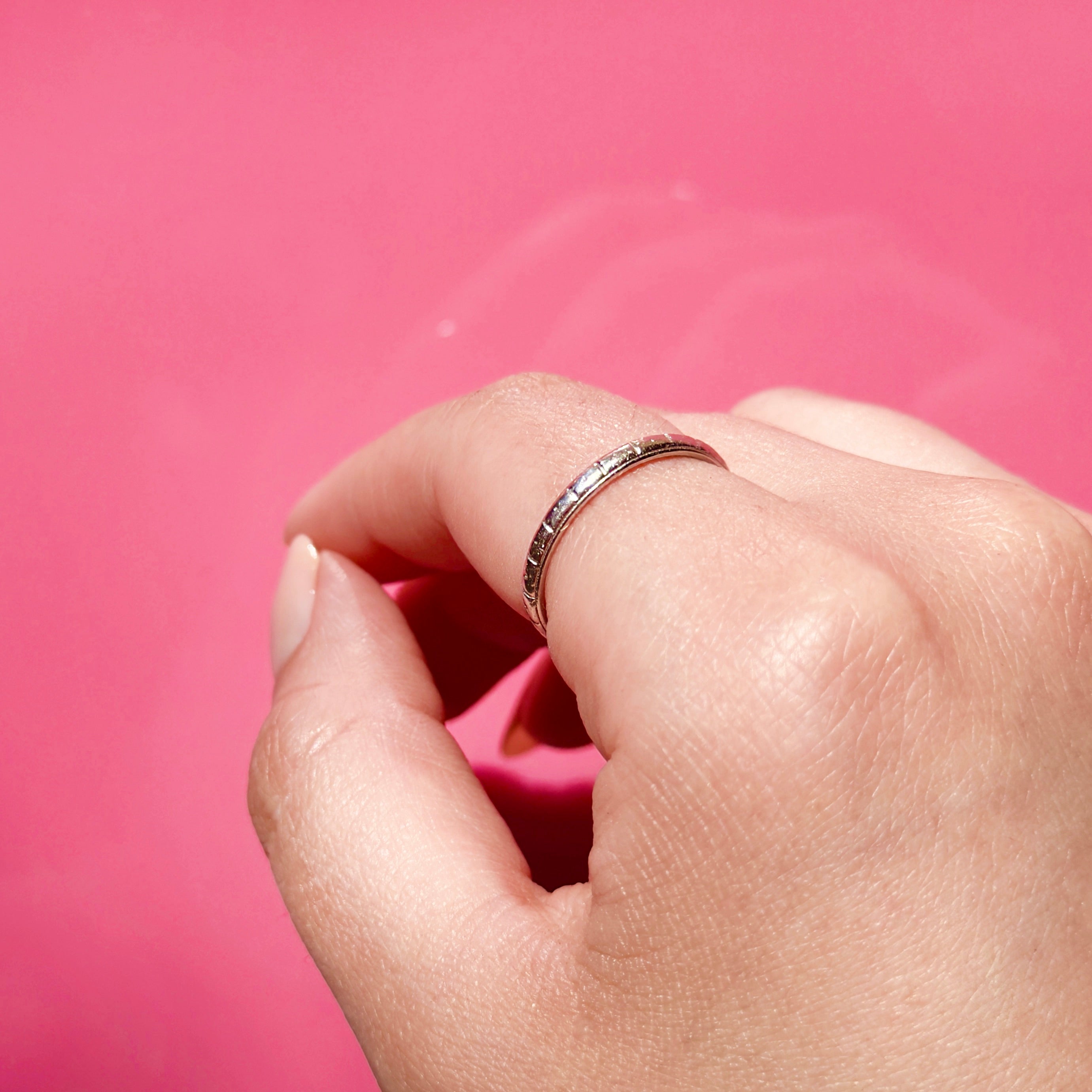 Hand wearing an antique platinum ring on a pink background
